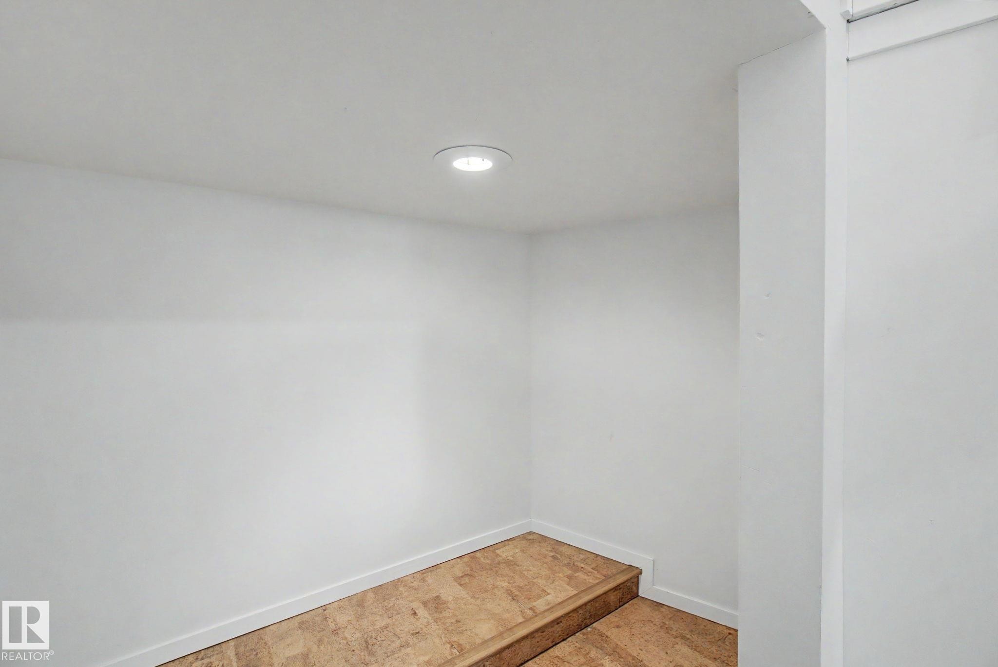 Recessed lighting illuminates a raised platform with wood-finish flooring, bordered by white baseboards - 11150 83 Avenue Nw, Edmonton, AB