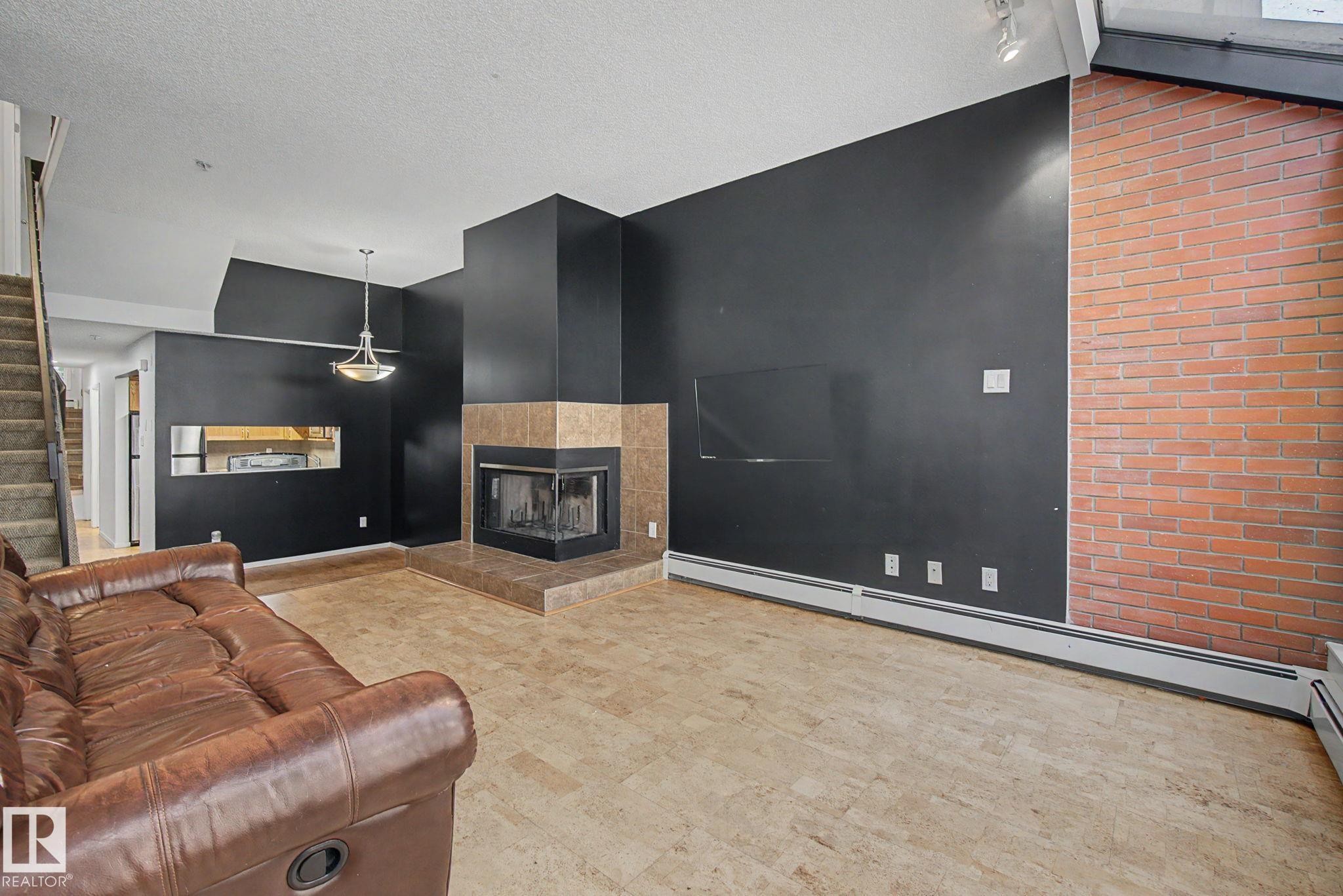 Living area featuring a corner fireplace with a tile surround and hearth, an exposed brick wall, and resilient flooring - 11150 83 Avenue Nw, Edmonton, AB