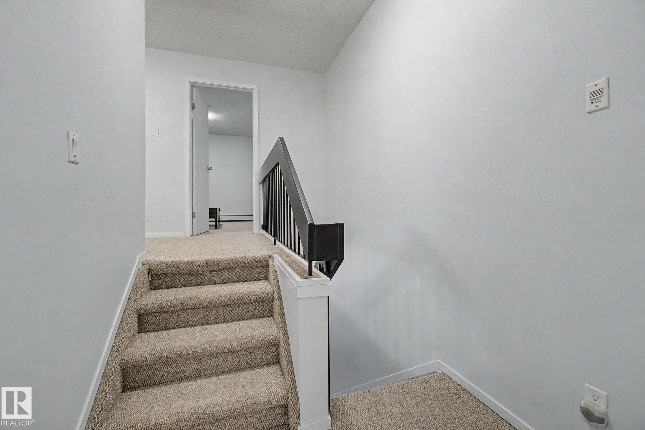 Carpeted staircase with white risers and a black metal and white wood railing - 11150 83 Avenue Nw, Edmonton, AB