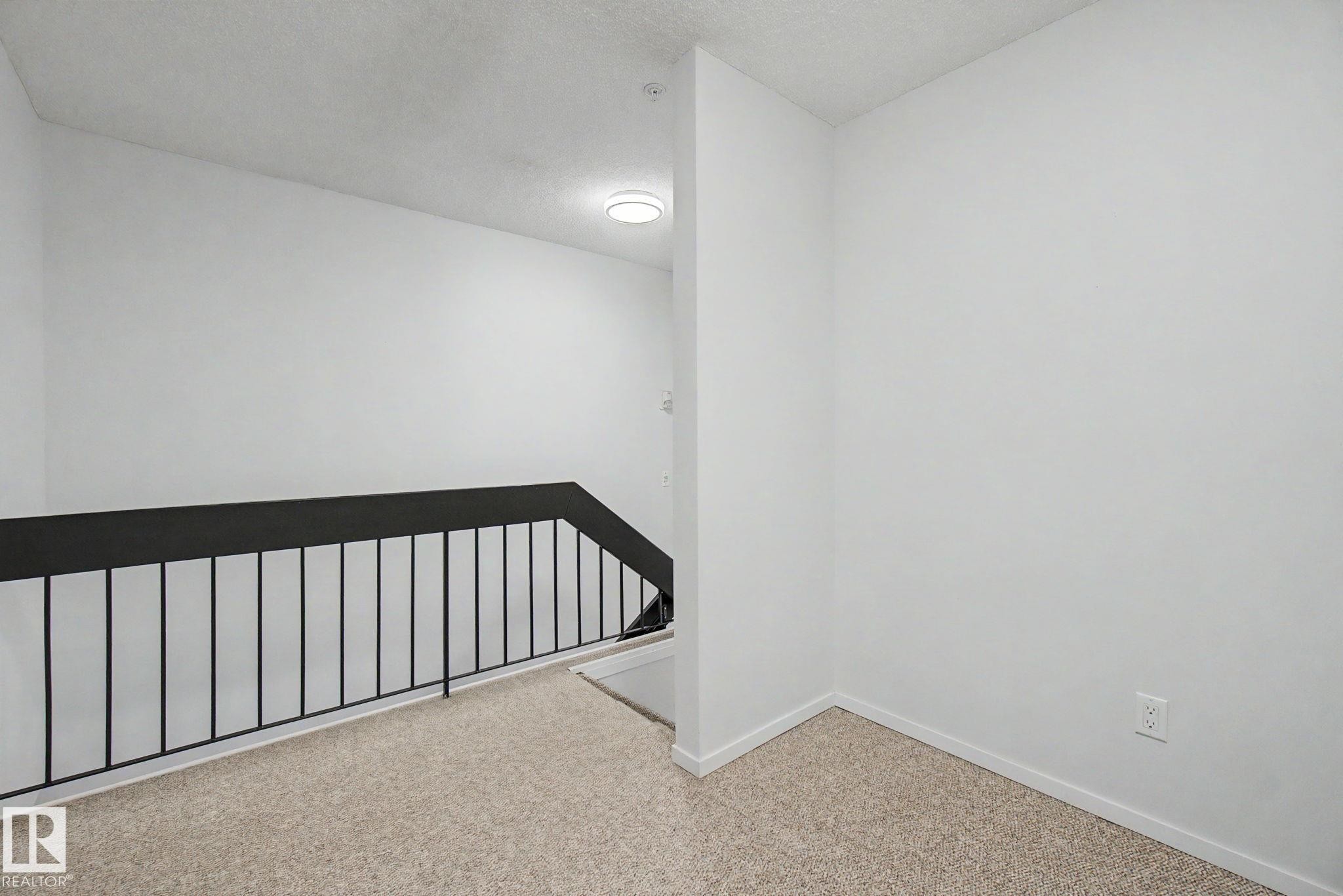 Stairwell with black metal railing and light-toned carpet flooring - 11150 83 Avenue Nw, Edmonton, AB