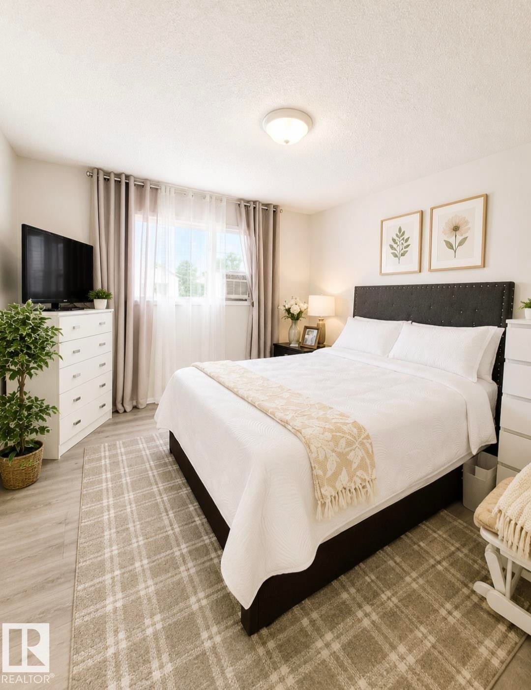 Light wood-finish flooring with a plaid area rug, featuring a window with sheer and solid drapes, and a flush-mount ceiling light fixture - 3236 27 Avenue Nw, Edmonton, AB - Indoor Photo Showing Bedroom