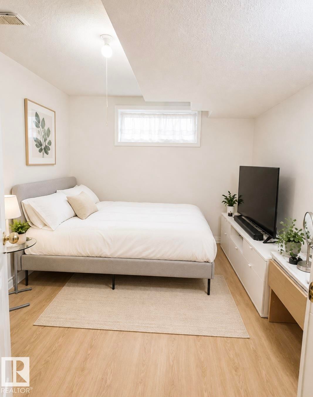 Bedroom featuring light wood-finish flooring, a neutral color palette, and a window with white sheer curtains - 3236 27 Avenue Nw, Edmonton, AB - Indoor Photo Showing Bedroom