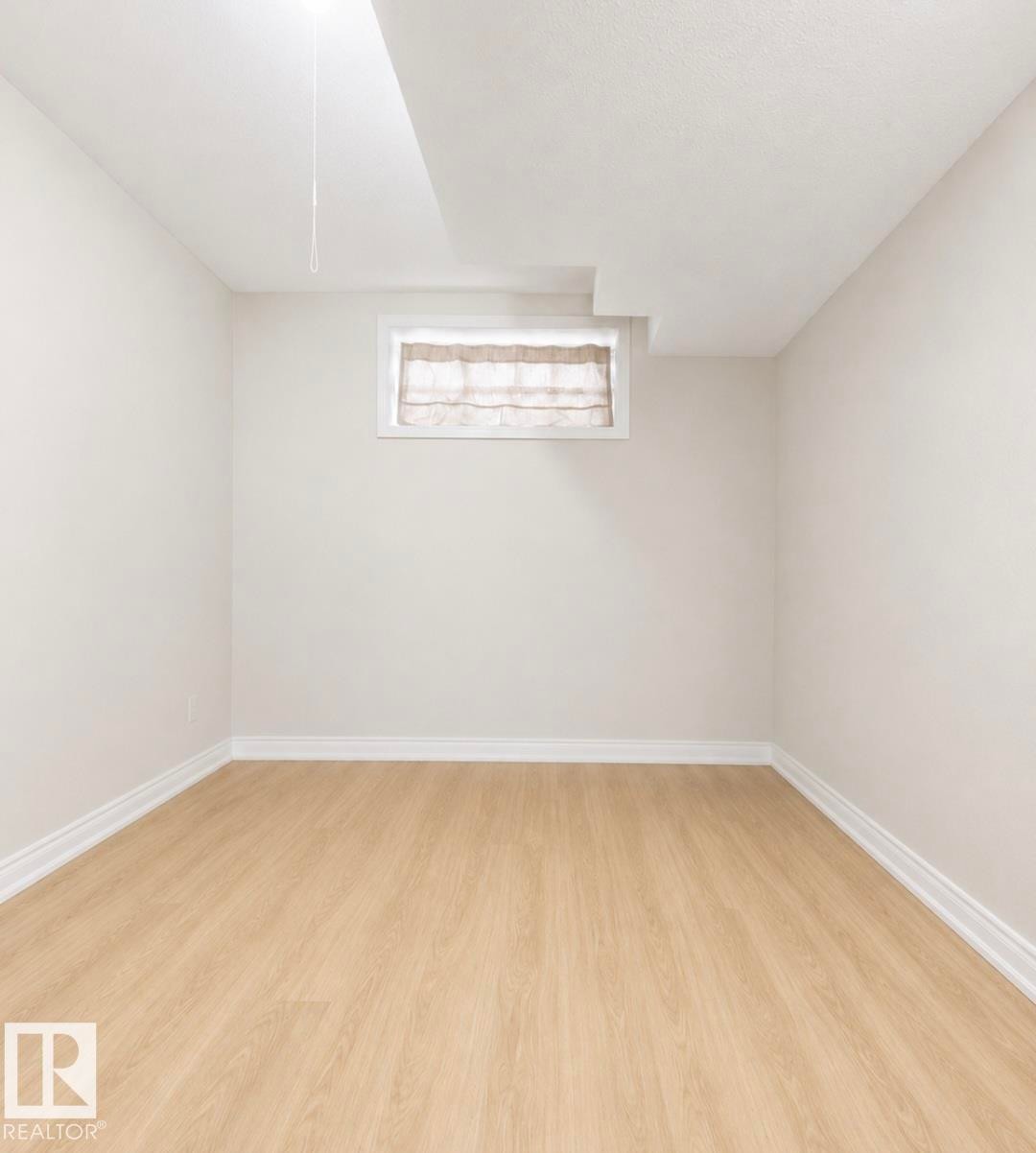 Light wood-finish flooring with crisp white baseboards and neutral wall tones - 3236 27 Avenue Nw, Edmonton, AB - Indoor Photo Showing Other Room