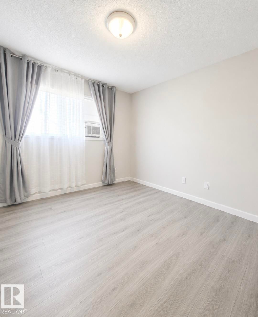 Room featuring light wood-finish flooring, a window with an integrated air conditioning unit, and a flush-mount ceiling light - 3236 27 Avenue Nw, Edmonton, AB - Indoor Photo Showing Other Room