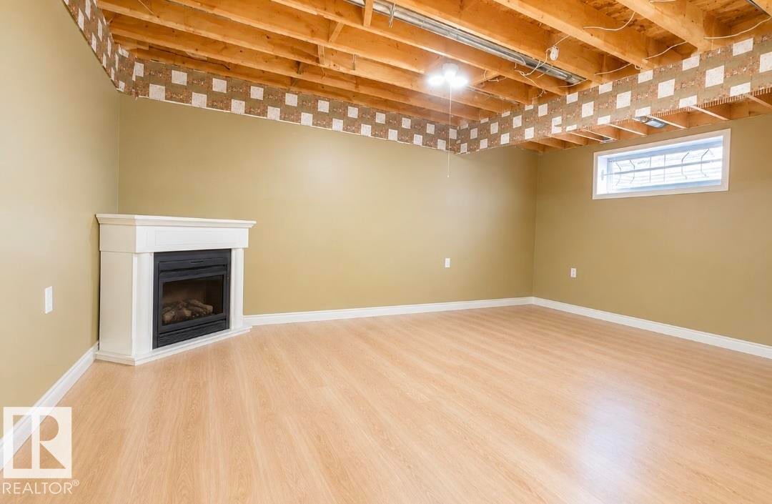 Corner fireplace with white mantel, light wood-finish flooring, and neutral wall paint - 3236 27 Avenue Nw, Edmonton, AB - Indoor Photo Showing Basement