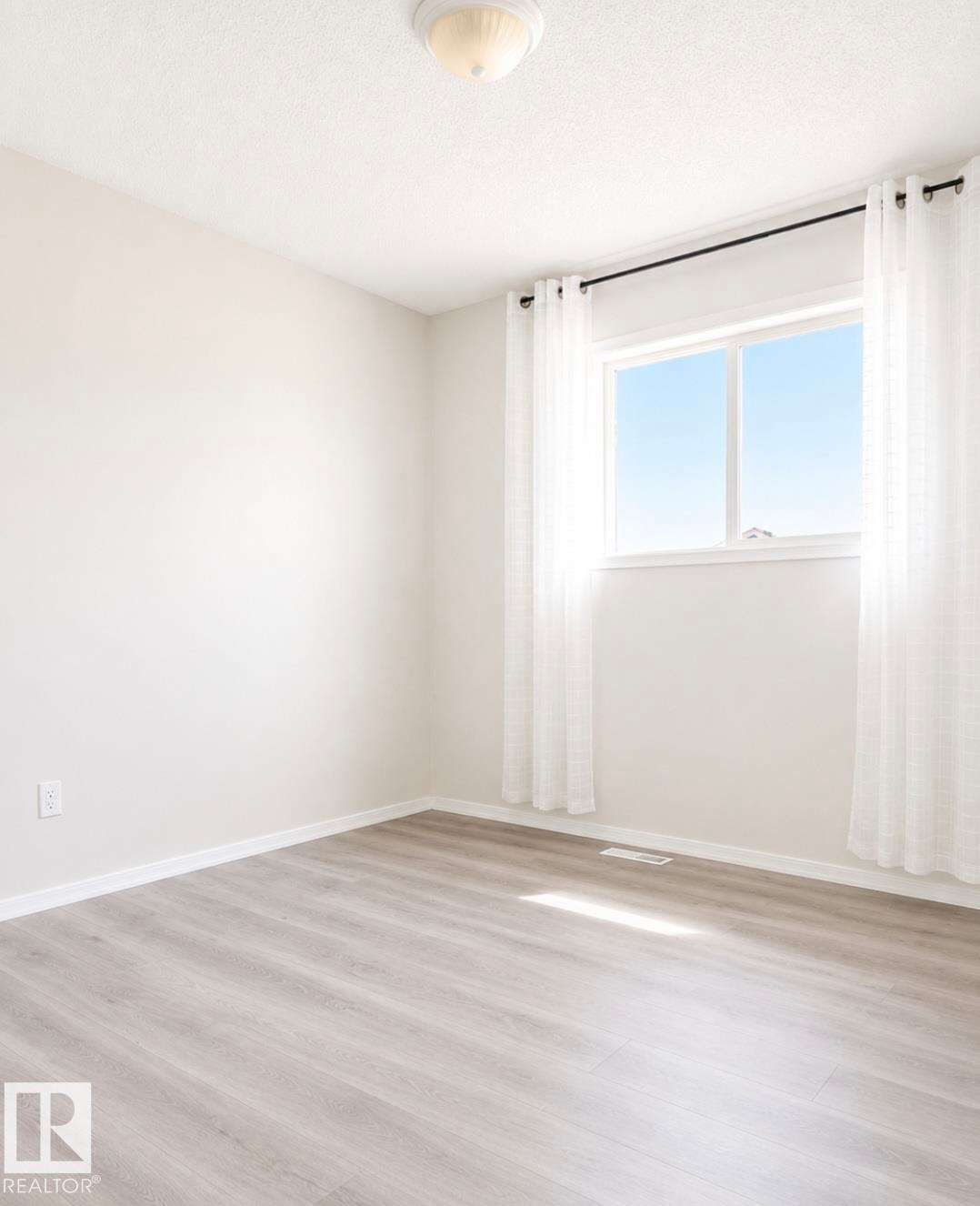Bright room featuring wood-finish flooring, a double-pane window with white trim, and a ceiling-mounted light fixture - 3236 27 Avenue Nw, Edmonton, AB - Indoor Photo Showing Other Room