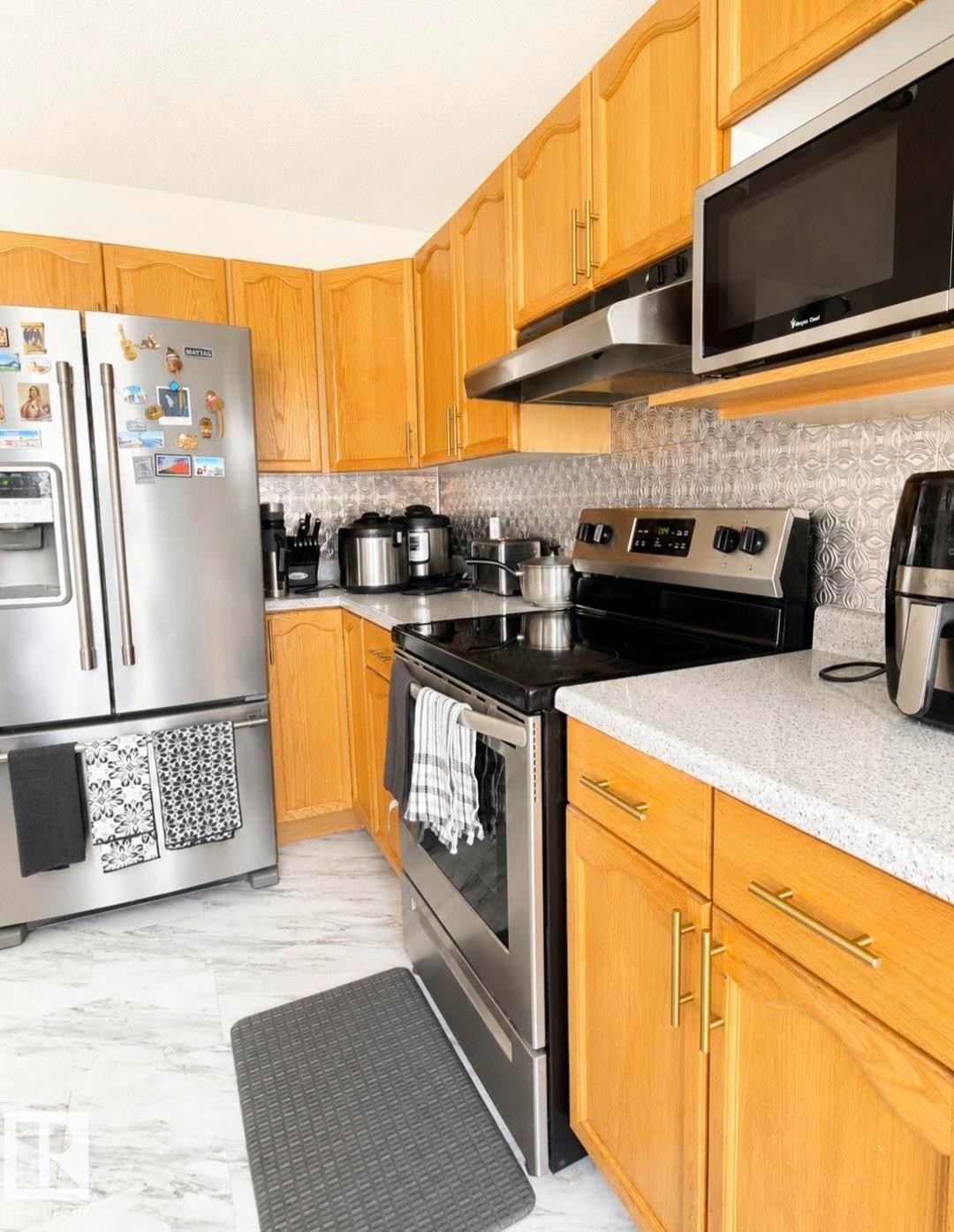 Kitchen featuring wood cabinetry, stainless steel appliances, speckled countertops, and a decorative backsplash - 3236 27 Avenue Nw, Edmonton, AB - Indoor Photo Showing Kitchen