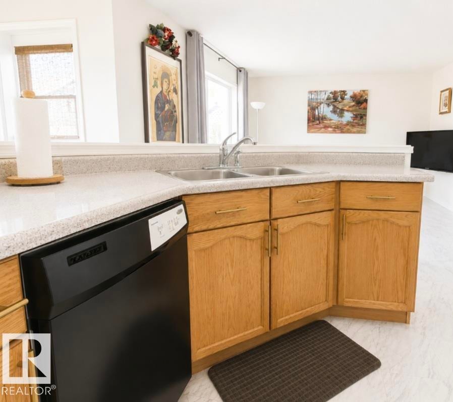 Kitchen featuring light wood cabinetry with gold-tone hardware, a stainless steel double basin sink, and a black dishwasher - 3236 27 Avenue Nw, Edmonton, AB - Indoor Photo Showing Kitchen With Double Sink