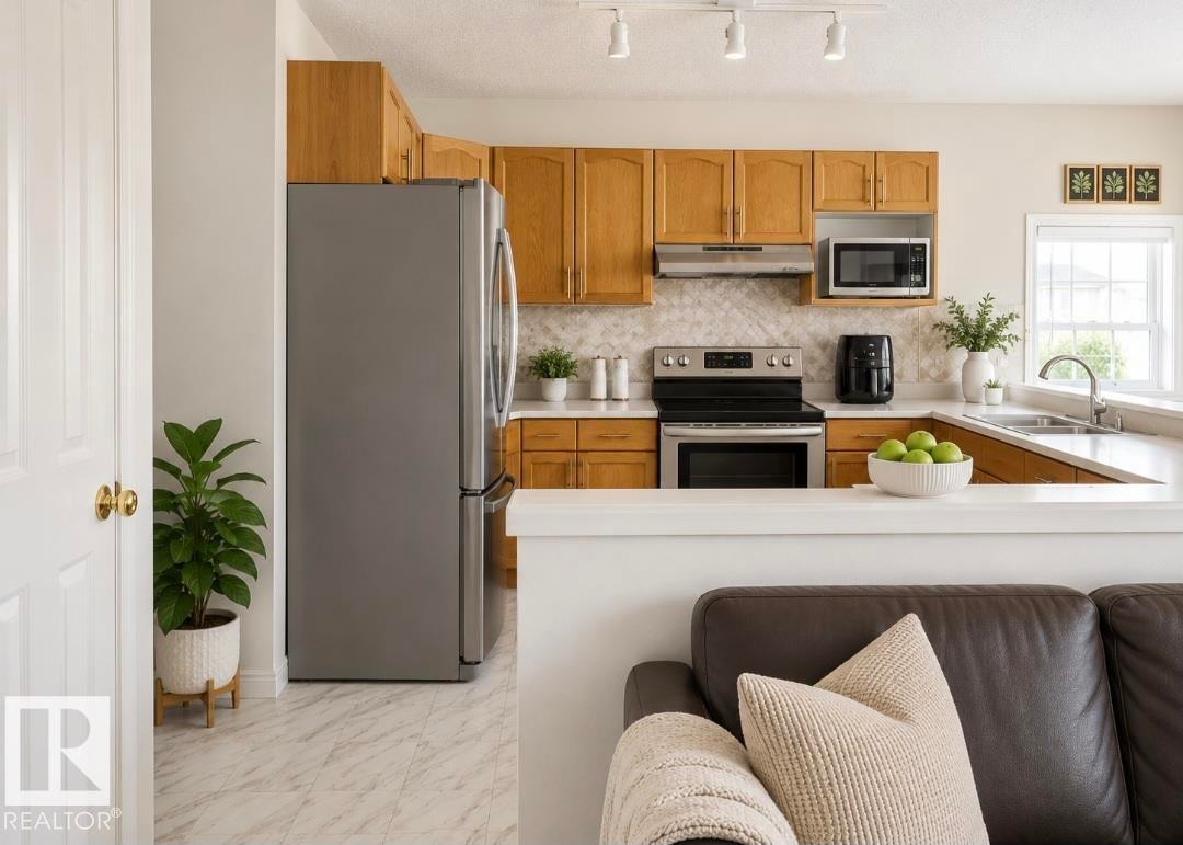Kitchen with wood-finish cabinetry, stainless steel appliances, white countertops, and a patterned backsplash - 3236 27 Avenue Nw, Edmonton, AB - Indoor Photo Showing Kitchen With Double Sink