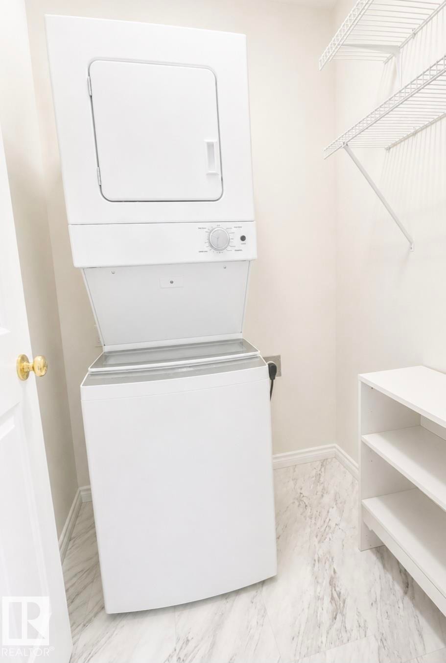 Laundry area featuring a stackable washer and dryer unit, white wire shelving, a white cubby organizer, and light-toned, veined flooring - 3236 27 Avenue Nw, Edmonton, AB - Indoor Photo Showing Laundry Room