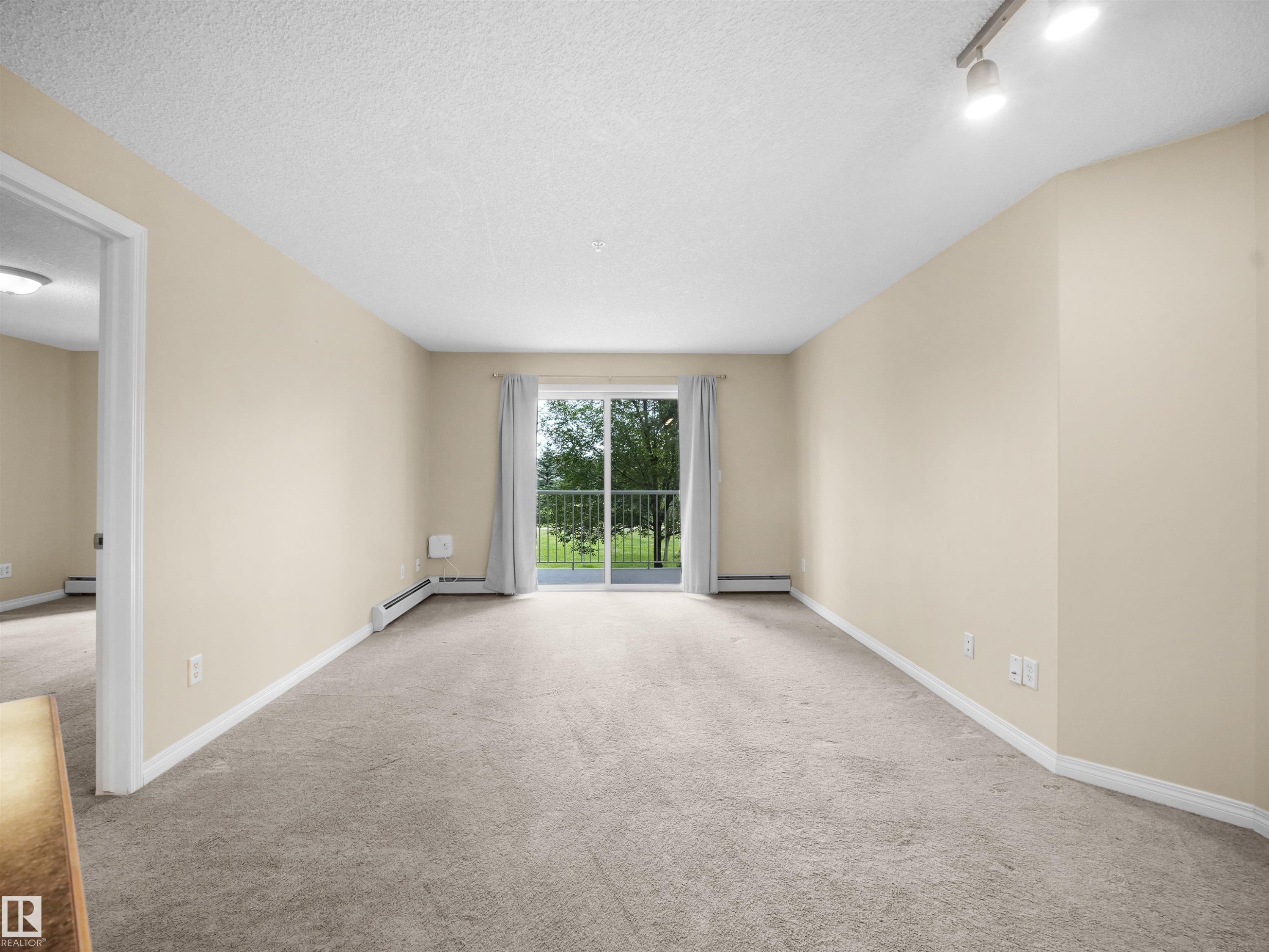 Sliding glass door leading to a balcony with metal railings - #220 245 Edwards Dr Sw, Edmonton, AB - Indoor Photo Showing Other Room