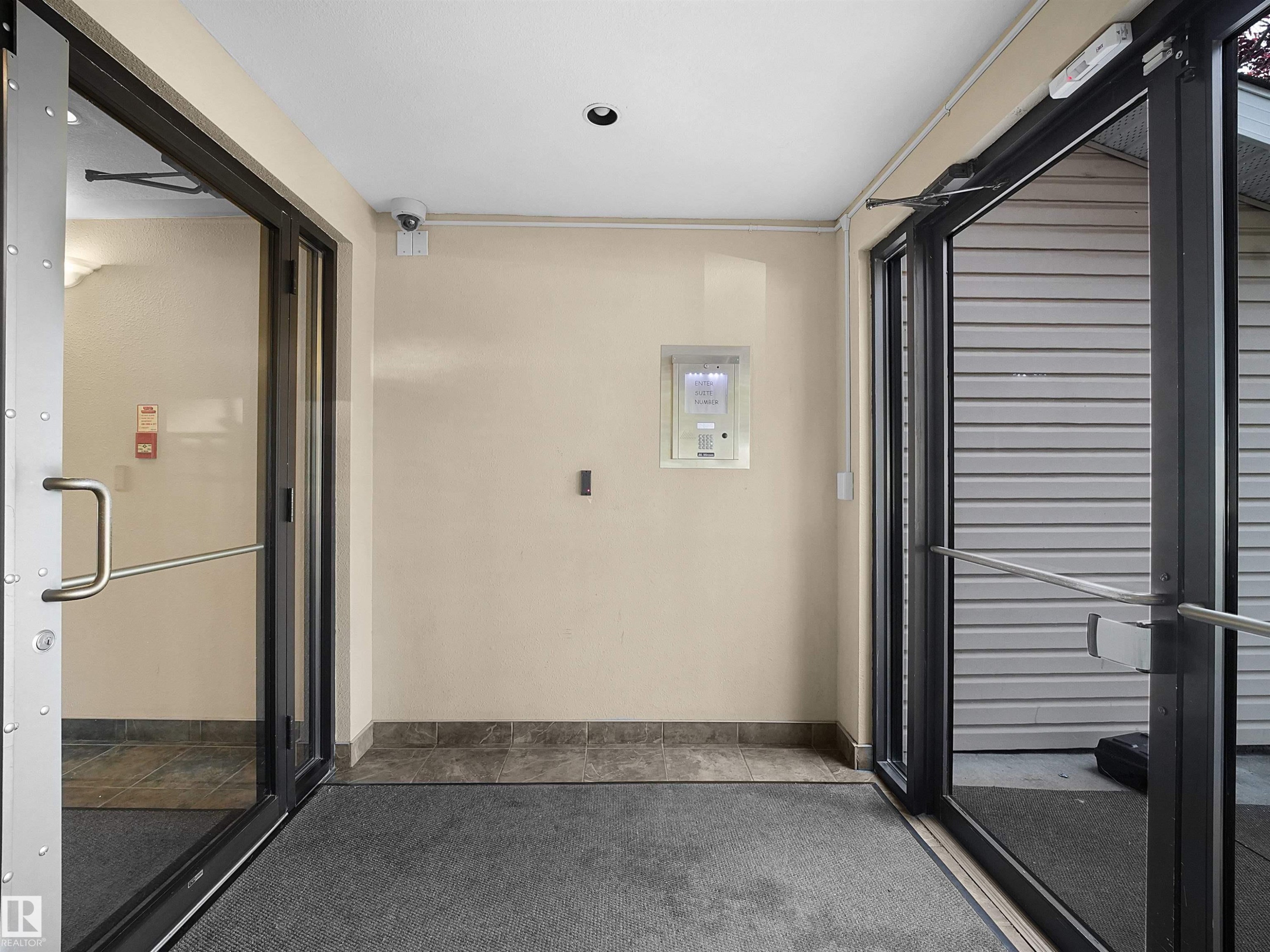 Entryway featuring double glass doors with metal frames and handles, recessed ceiling lighting, a security camera, and a tiled threshold - #220 245 Edwards Dr Sw, Edmonton, AB - Photo Showing Other Room