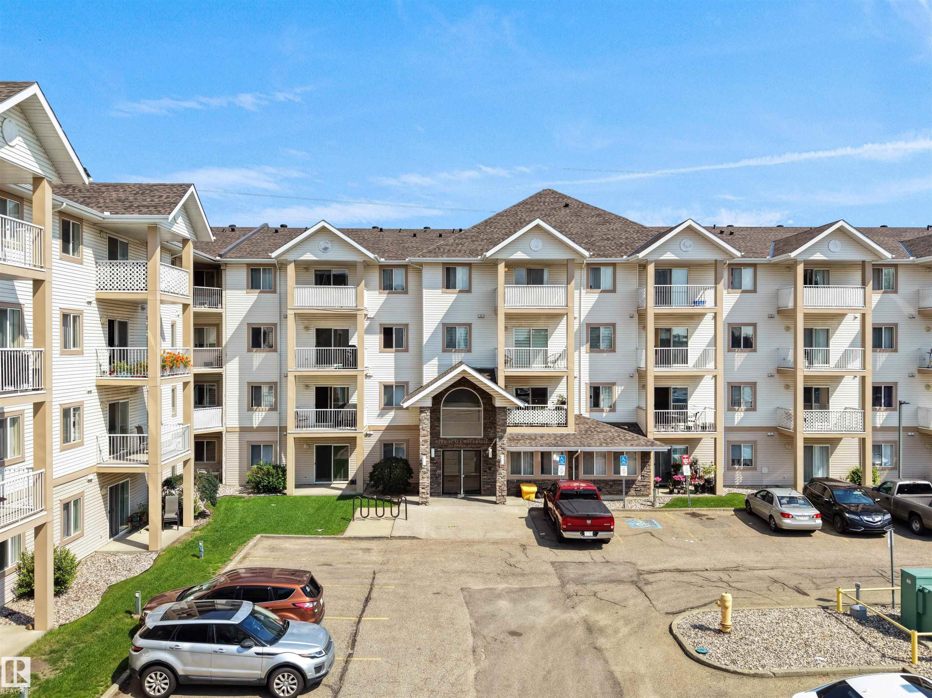 Multi-story residential building featuring balconies, an arched stone entrance, and asphalt parking - #220 245 Edwards Dr Sw, Edmonton, AB - Outdoor With Balcony With Facade