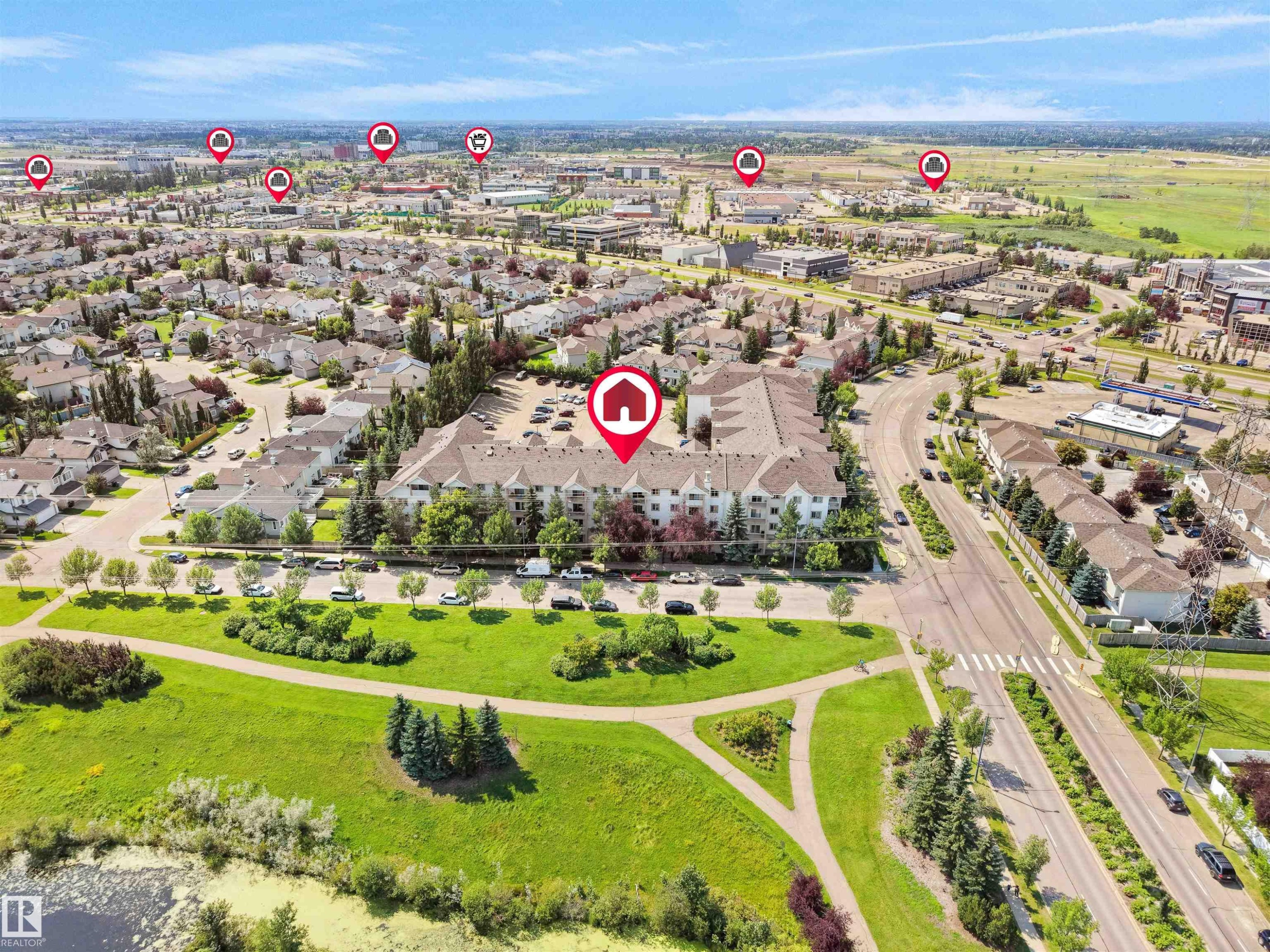 Aerial perspective showcasing a multi-story residential building with surface parking, bordering a green space with walking paths and a body of water - #220 245 Edwards Dr Sw, Edmonton, AB - Outdoor With View