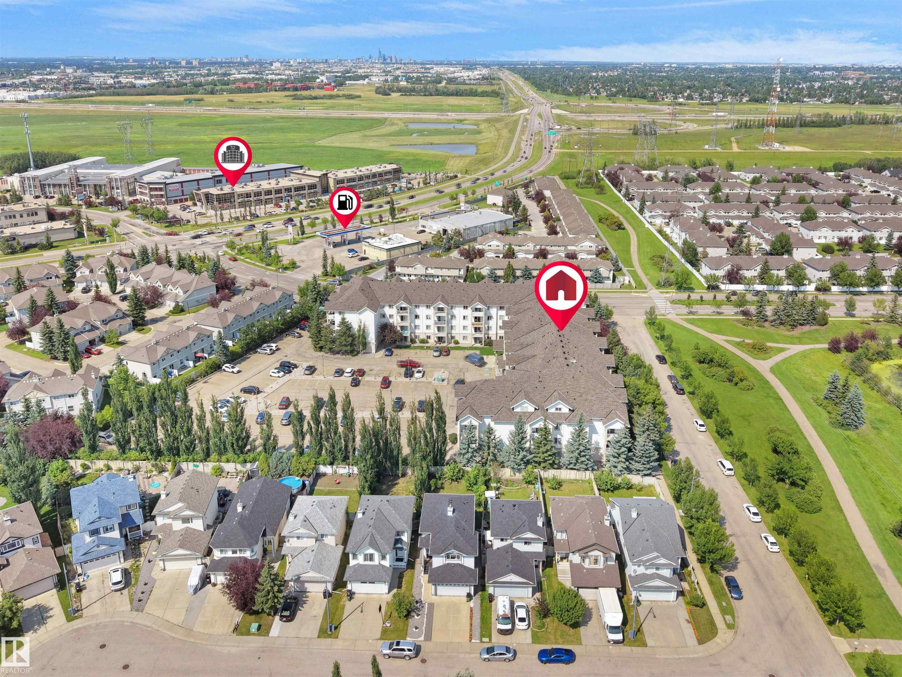 Aerial perspective showcasing residential properties including detached homes and multi-story buildings, alongside a highway and green spaces - #220 245 Edwards Dr Sw, Edmonton, AB - Outdoor With View