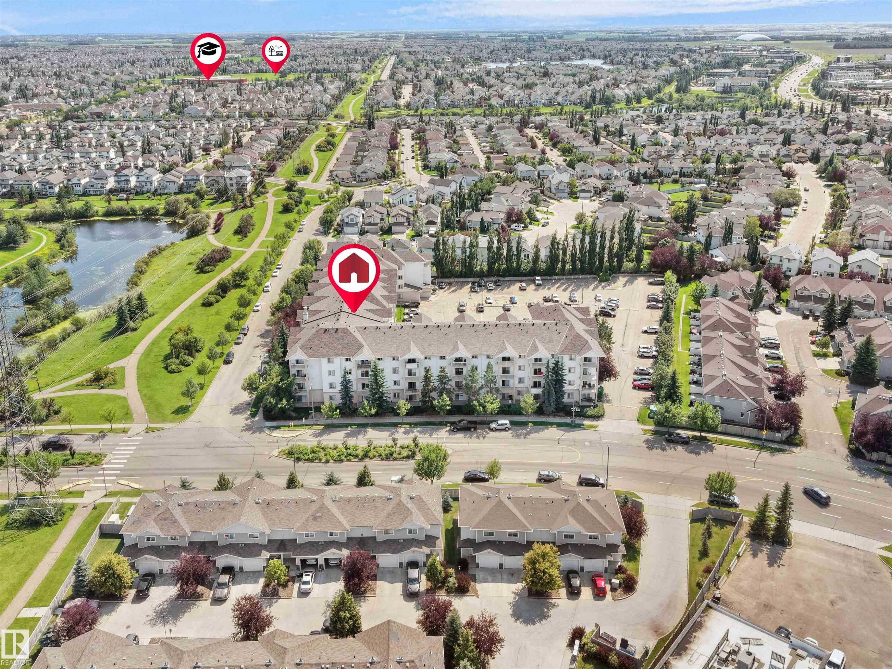 Aerial perspective showcasing a multi-story residential building with ample surface parking - #220 245 Edwards Dr Sw, Edmonton, AB - Outdoor With View