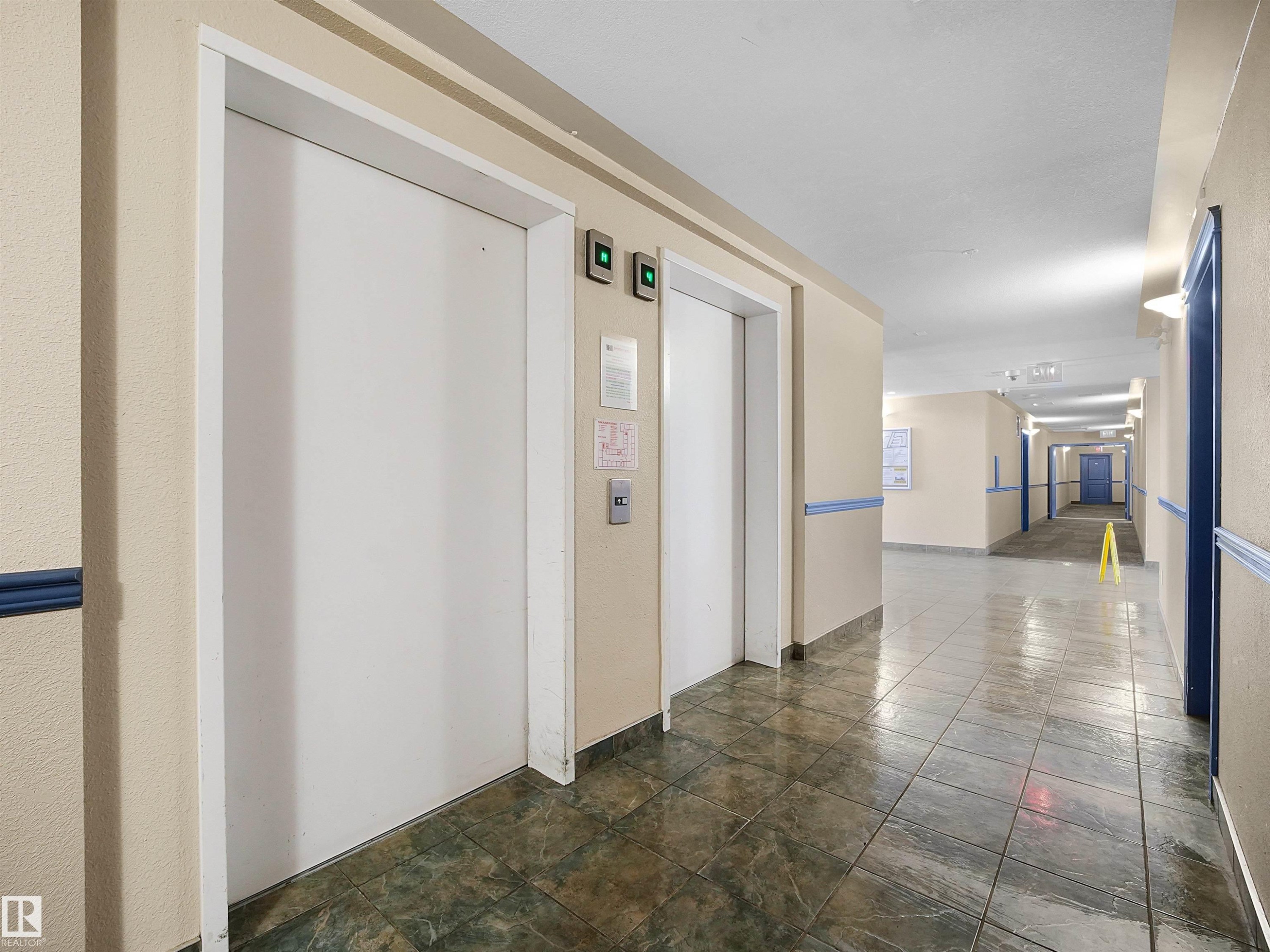 Two white elevator doors with call buttons, set against a cream-colored wall - #220 245 Edwards Dr Sw, Edmonton, AB - Indoor Photo Showing Other Room