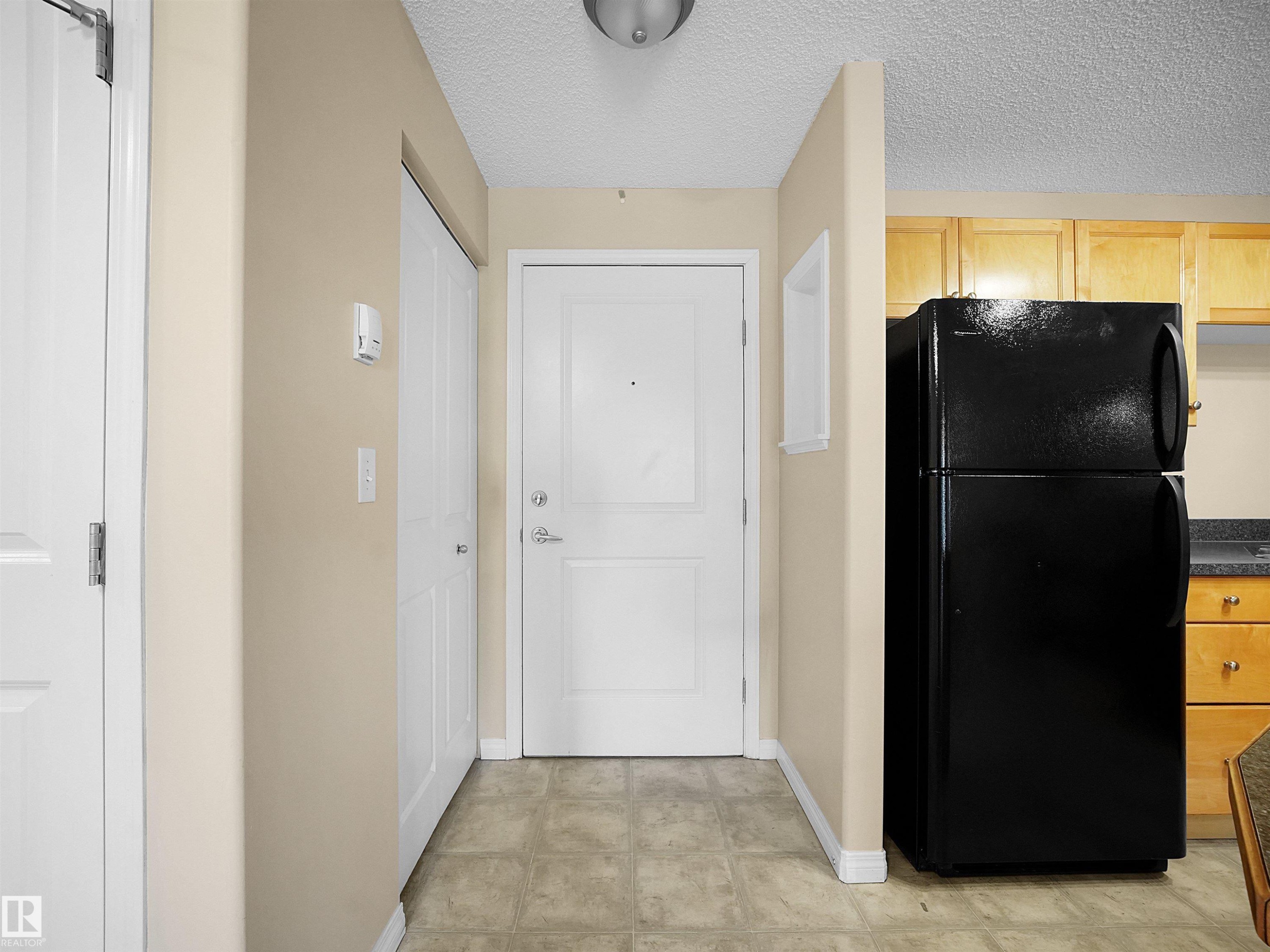 Hallway entry featuring neutral taupe walls, white trim, and neutral-tone tile flooring - #220 245 Edwards Dr Sw, Edmonton, AB - Indoor Photo Showing Other Room