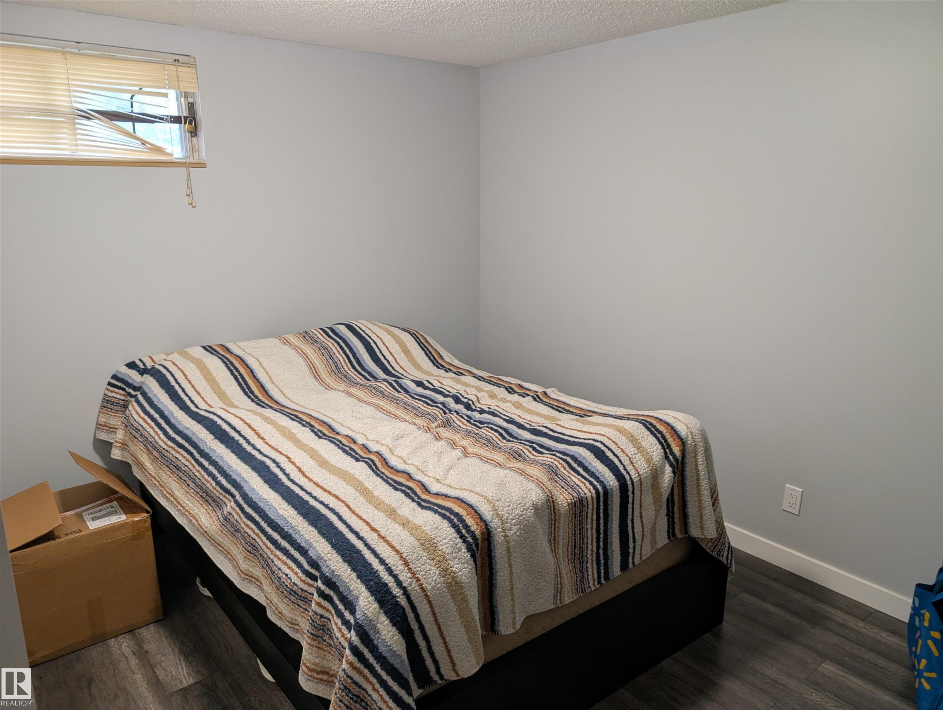 Room featuring wood-finish flooring, a window with blinds, light-colored walls, white baseboards, and a textured ceiling - 14228 22 Street Nw, Edmonton, AB - Indoor Photo Showing Bedroom