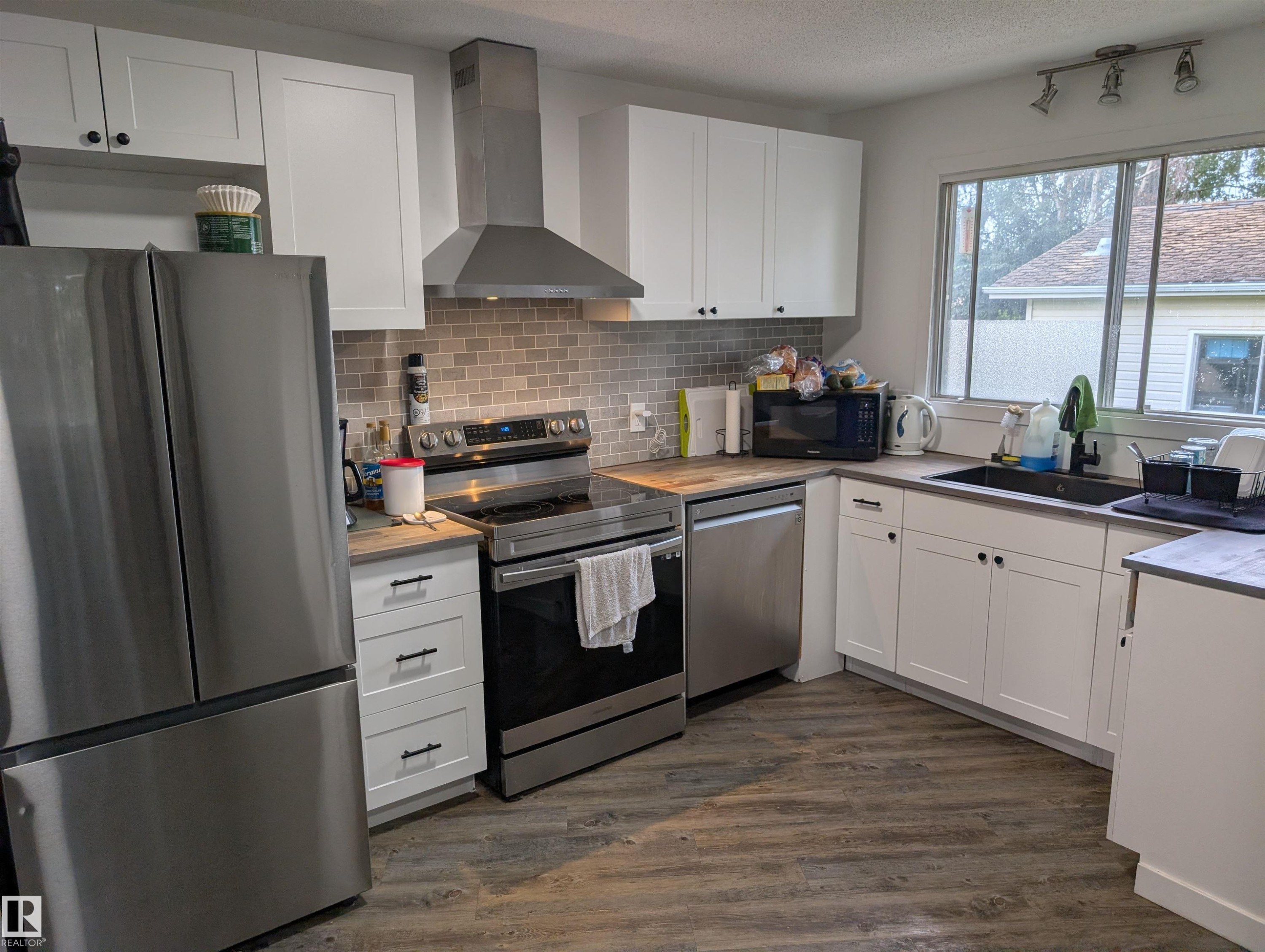 Kitchen featuring white shaker-style cabinetry, wood-finish countertops, stainless steel appliances, a tile backsplash, and wood-finish flooring - 14228 22 Street Nw, Edmonton, AB - Indoor Photo Showing Kitchen With Double Sink