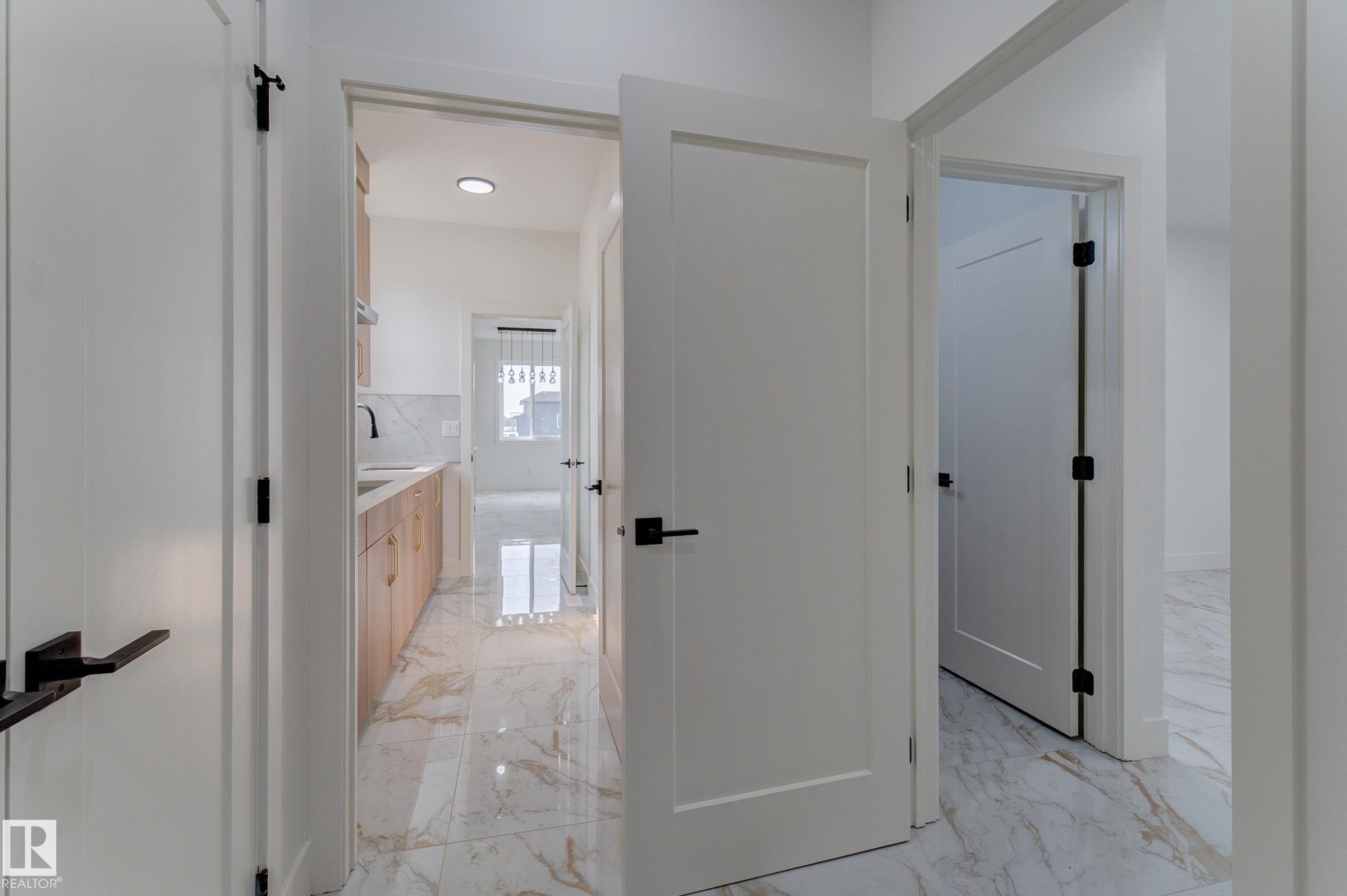 Hallway entry featuring white paneled doors with matte black hardware, leading to a utility space with wood-finish cabinetry, a white countertop, a black faucet, and a white tile backsplash - 4723 17 Avenue Sw, Edmonton, AB - Indoor Photo Showing Other Room