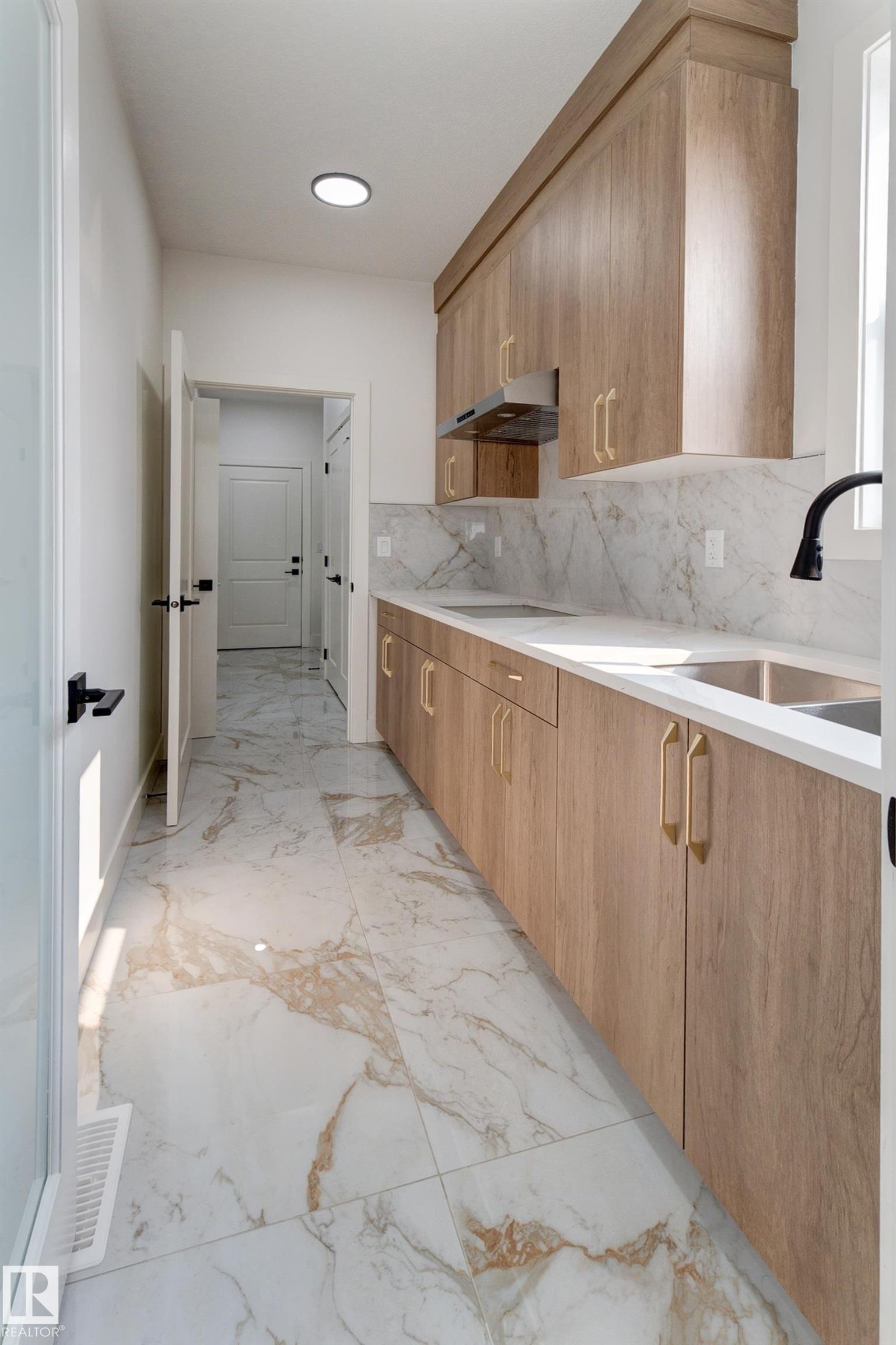 Contemporary galley kitchen featuring wood-finish cabinetry with gold-tone hardware, white countertops, and a white and gold patterned tile backsplash - 4723 17 Avenue Sw, Edmonton, AB - Indoor Photo Showing Kitchen