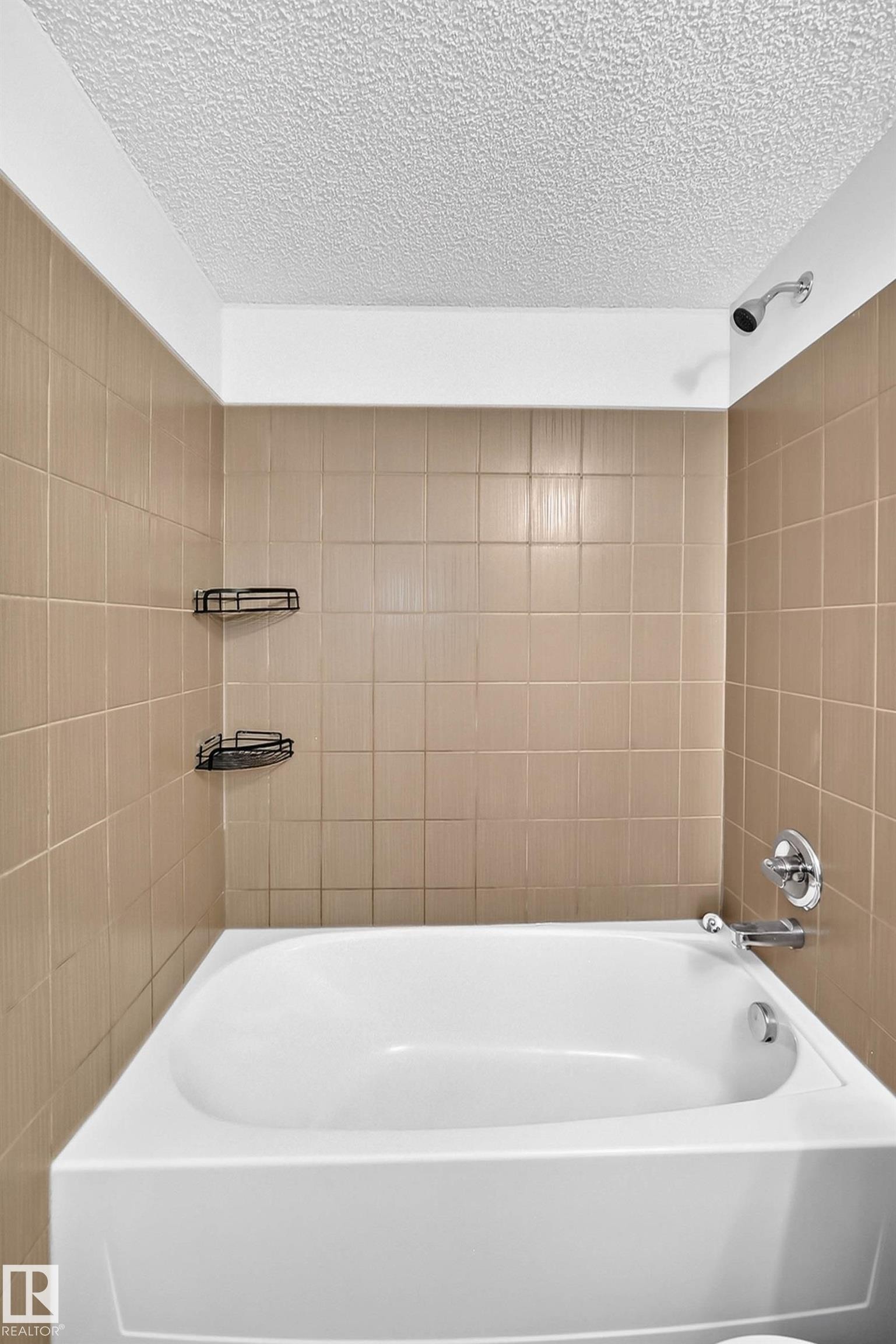 White bathtub with chrome fixtures, surrounded by light brown square wall tiles - #404 12025 22 Av Sw, Edmonton, AB - Indoor Photo Showing Bathroom