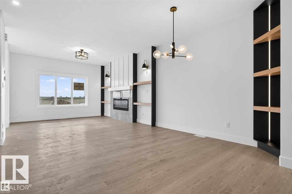 Spacious room featuring wood-finish flooring, a modern fireplace with a stone surround, and built-in shelving with integrated lighting - 43 River Birch Way, St. Albert, AB - Indoor