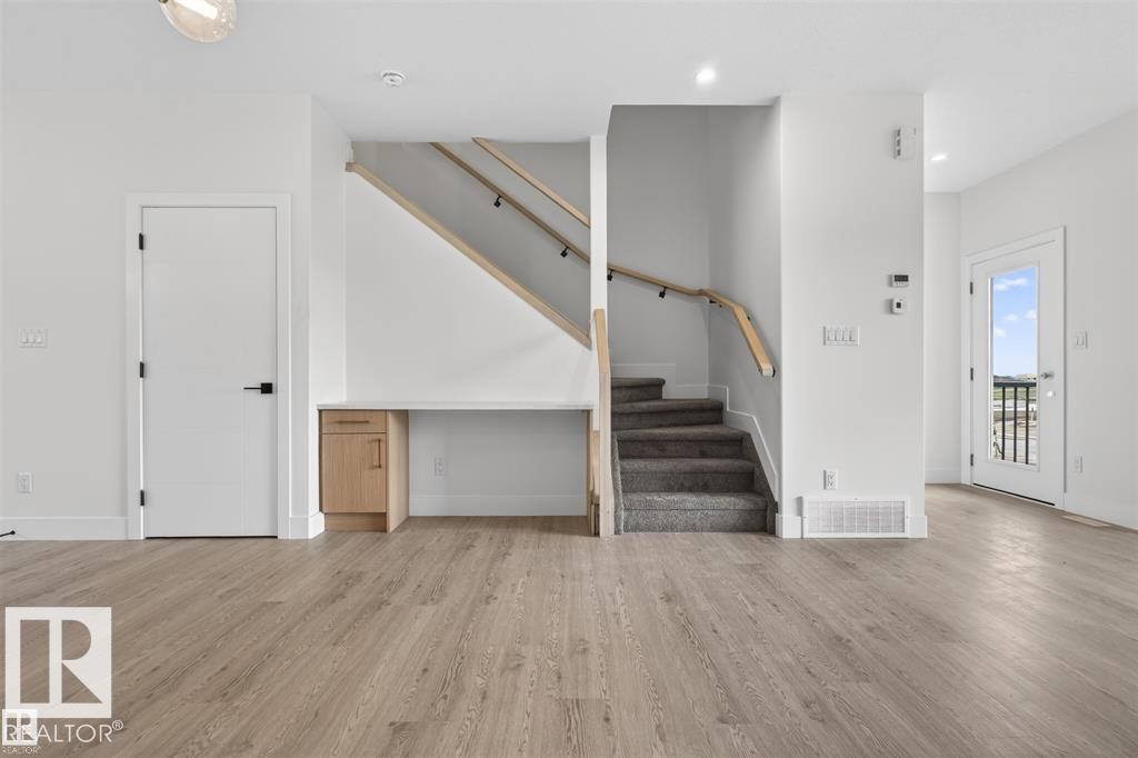 Open concept interior featuring wide plank wood-finish flooring, a built-in desk with natural wood cabinetry, and a carpeted staircase with light wood handrails - 43 River Birch Way, St. Albert, AB - Indoor Photo Showing Other Room