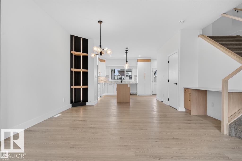 Open-concept living space featuring light wood-finish flooring, a built-in shelving unit with dark paneling, and contemporary lighting fixtures - 43 River Birch Way, St. Albert, AB - Indoor