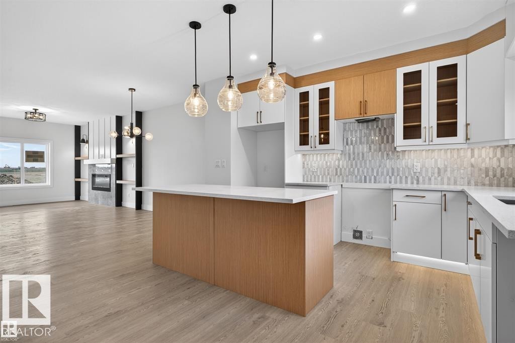 Open-concept kitchen and living area featuring a central island with wood-finish paneling, white countertops, and three pendant light fixtures - 43 River Birch Way, St. Albert, AB - Indoor Photo Showing Kitchen With Upgraded Kitchen