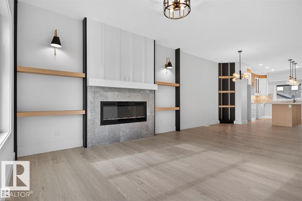 Living space featuring a linear electric fireplace with a textured surround, integrated wood-finish shelving, and light wood-finish flooring - 43 River Birch Way, St. Albert, AB - Indoor Photo Showing Living Room With Fireplace