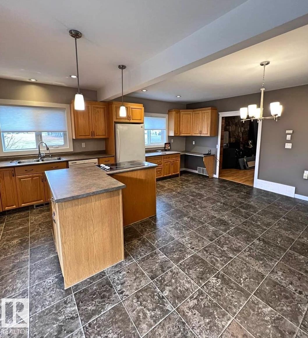 Spacious kitchen featuring an L-shaped island with a built-in cooktop, ample wood cabinetry, a double basin sink, and lino flooring. - 3003 Park Avenue, Mallaig, AB - Indoor Photo Showing Kitchen With Double Sink