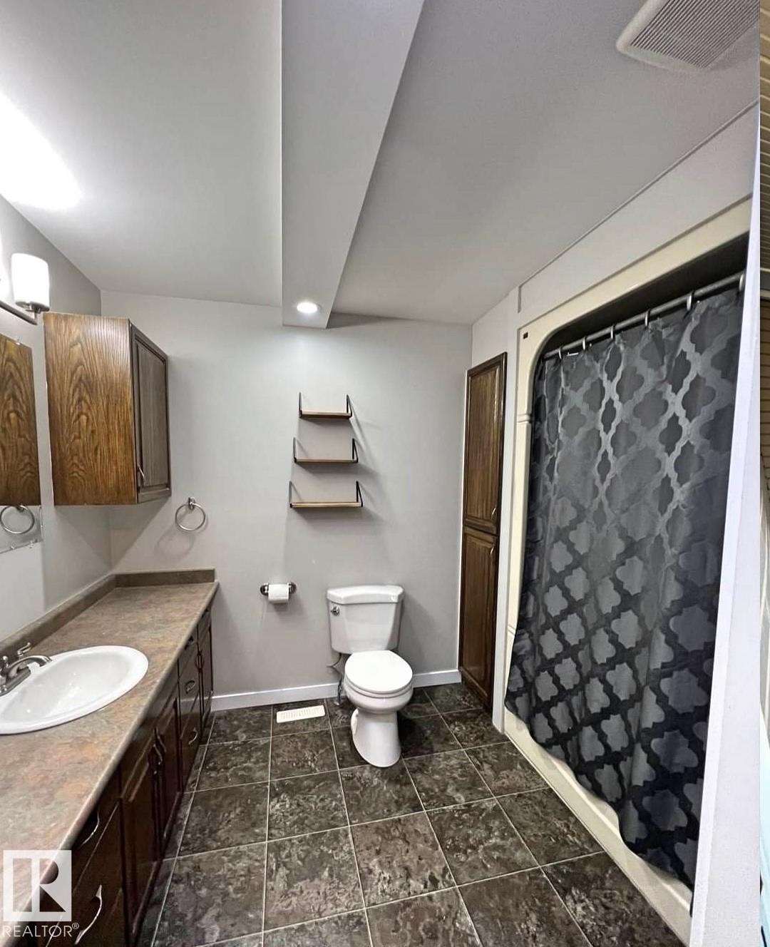 Bathroom featuring a built-in vanity with a white basin sink and wood-finish cabinetry, a toilet, and a shower with a white surround - 3003 Park Avenue, Mallaig, AB - Indoor Photo Showing Bathroom
