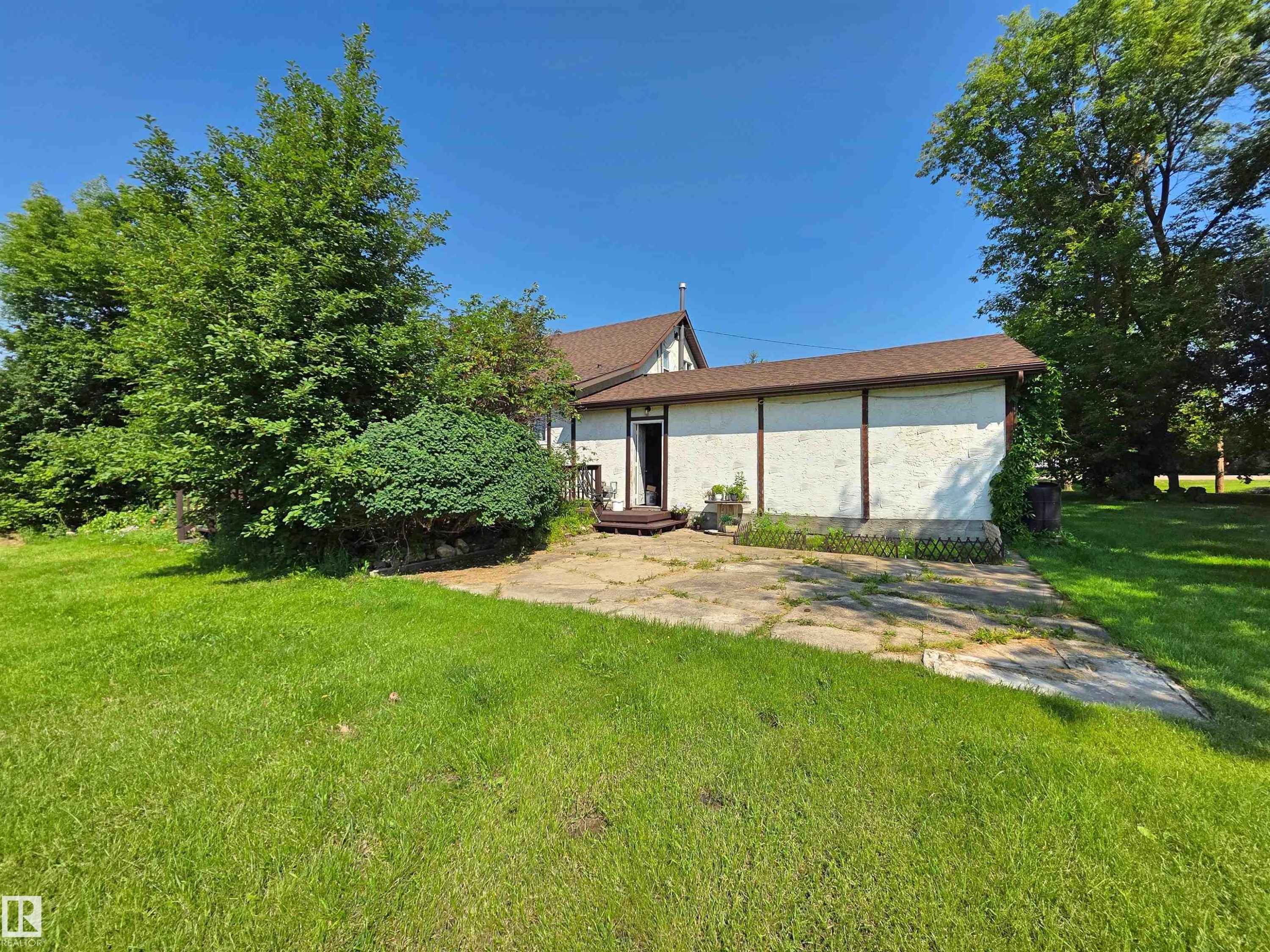 Expansive green lawn with mature trees and established shrubbery surrounding a concrete patio area - 3003 Park Avenue, Mallaig, AB - Outdoor