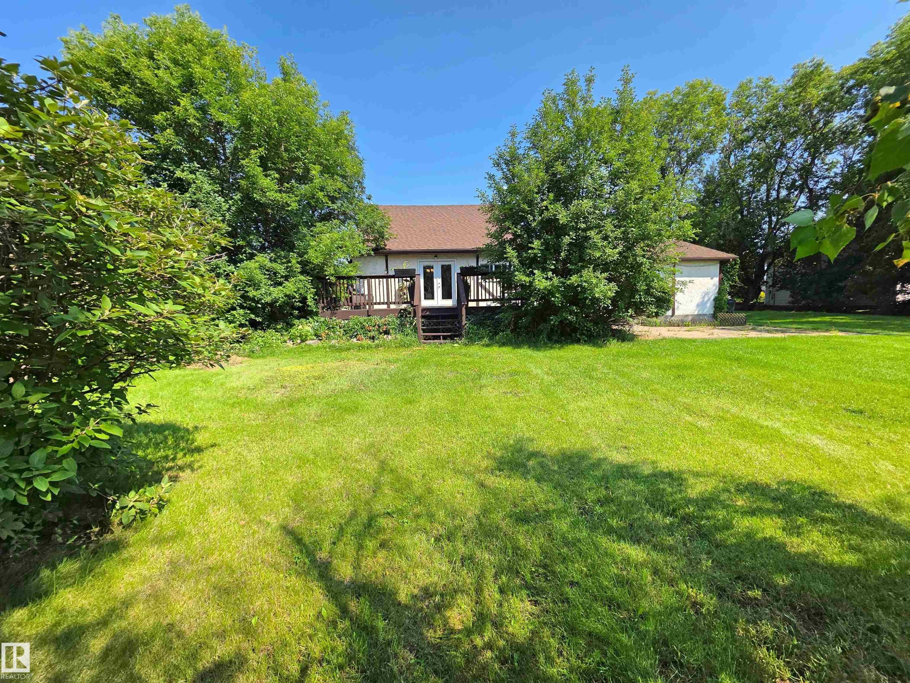 Expansive backyard with a large lawn, mature trees, and a spacious rear deck - 3003 Park Avenue, Mallaig, AB - Outdoor