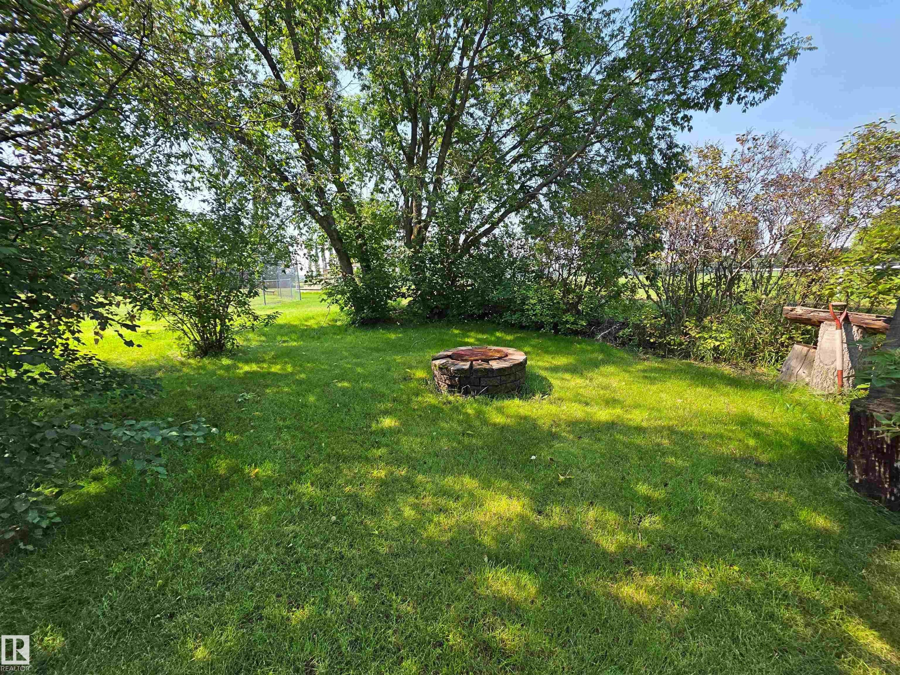 Expansive grassy yard featuring a fire pit, mature trees, and surrounding shrubbery - 3003 Park Avenue, Mallaig, AB - Outdoor