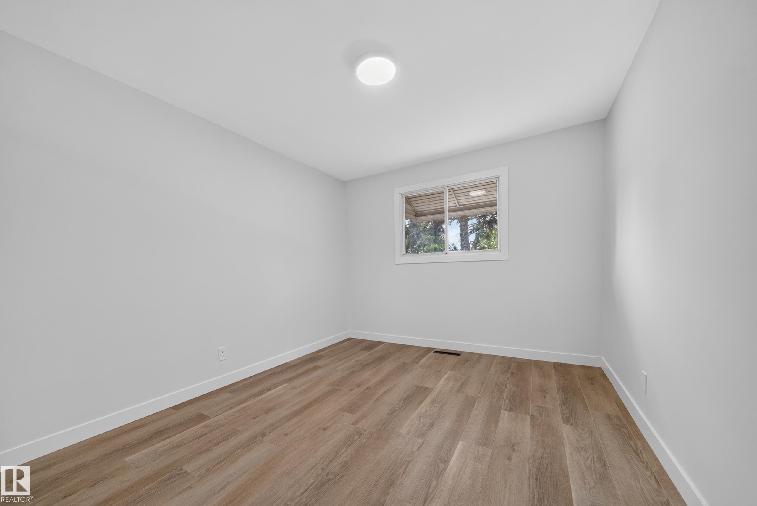 Light-filled interior space featuring wood-finish flooring, white baseboards, and a flush-mount ceiling light fixture - 5204 97A Avenue Nw, Edmonton, AB - Indoor Photo Showing Other Room