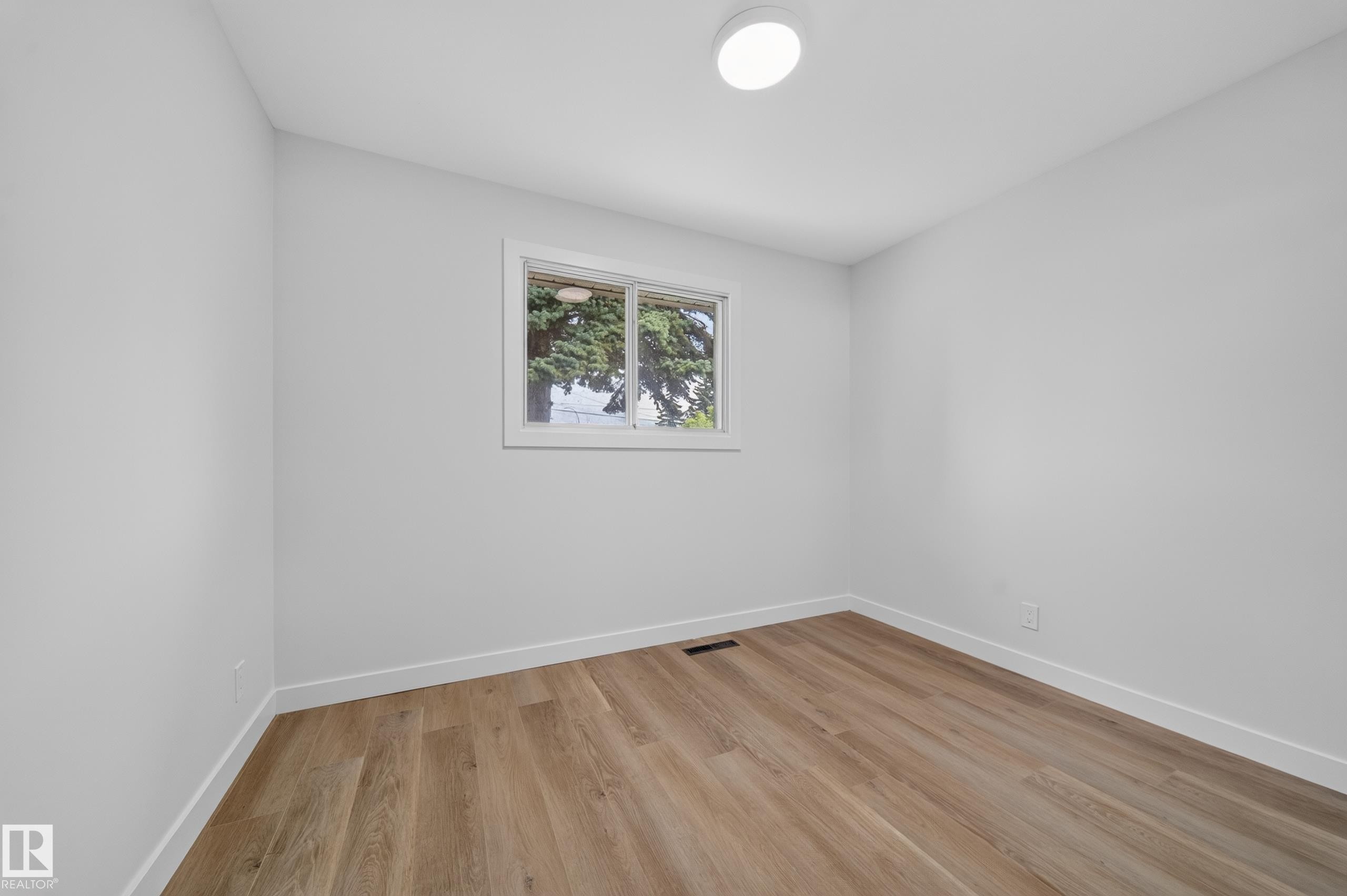 Room featuring wood-finish flooring, white baseboards, and a single window with white trim - 5204 97A Avenue Nw, Edmonton, AB - Indoor Photo Showing Other Room