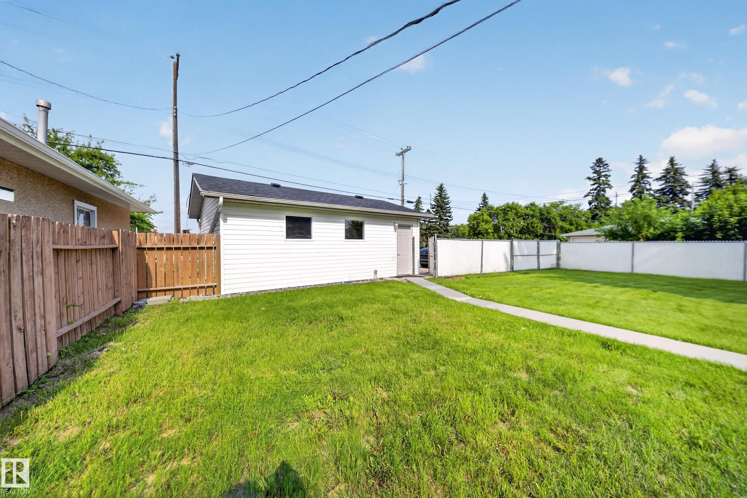 Spacious backyard featuring a detached garage with white siding, a concrete pathway, a wood privacy fence, and a white vinyl fence - 5204 97A Avenue Nw, Edmonton, AB - Outdoor