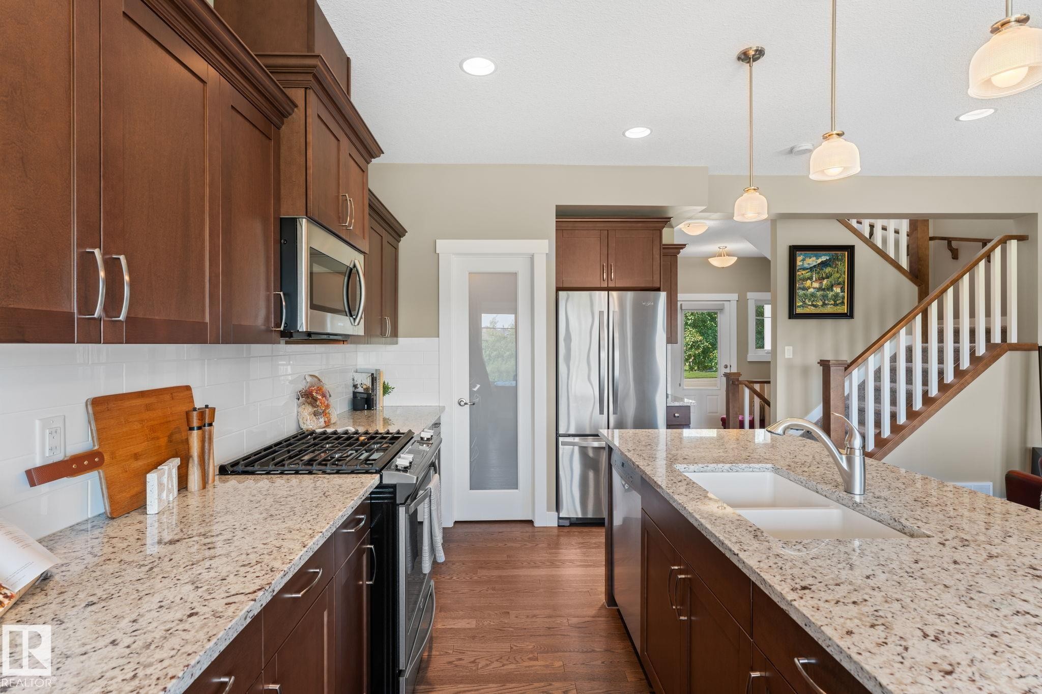 Kitchen featuring granite countertops, wood cabinetry, stainless steel appliances, and wood-finish flooring - 3413 Cameron Heights Cove Nw, Edmonton, AB - Indoor Photo Showing Kitchen With Double Sink With Upgraded Kitchen
