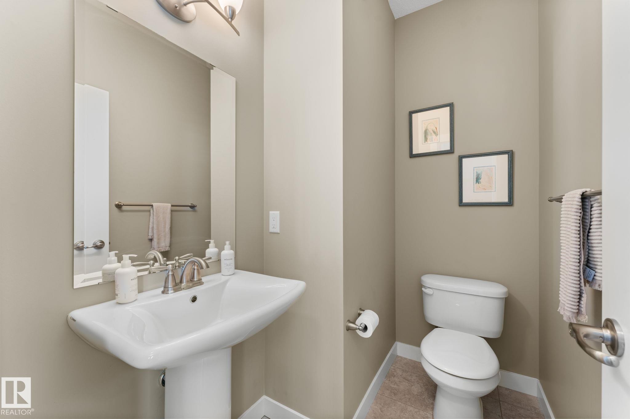 Powder room featuring a pedestal sink with brushed nickel faucet, large wall mirror, and tile flooring - 3413 Cameron Heights Cove Nw, Edmonton, AB - Indoor Photo Showing Bathroom