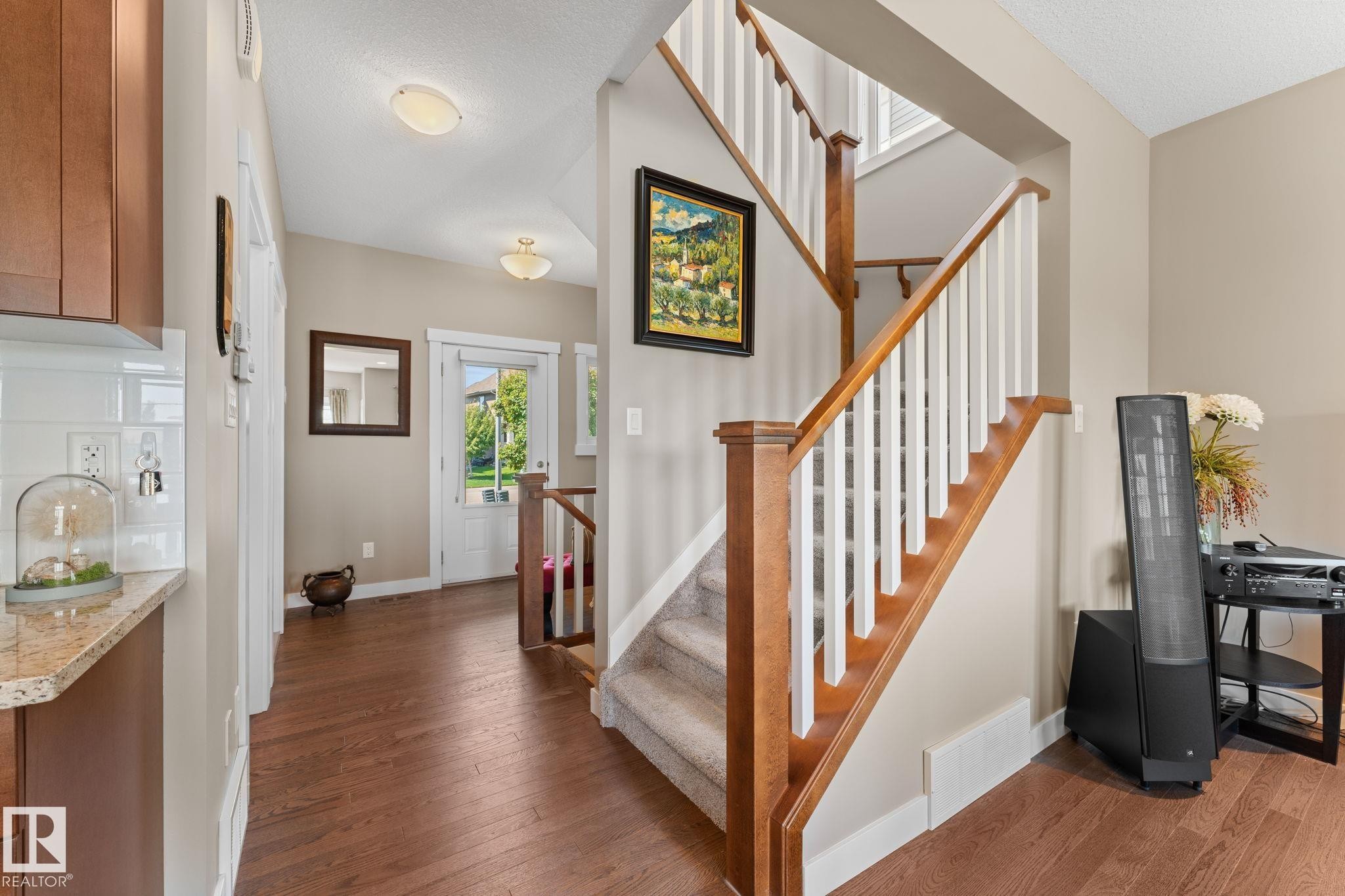 Foyer showcasing a wooden staircase with white balusters, wood-finish flooring, and a built-in kitchen cabinet with a light-toned countertop - 3413 Cameron Heights Cove Nw, Edmonton, AB - Indoor Photo Showing Other Room