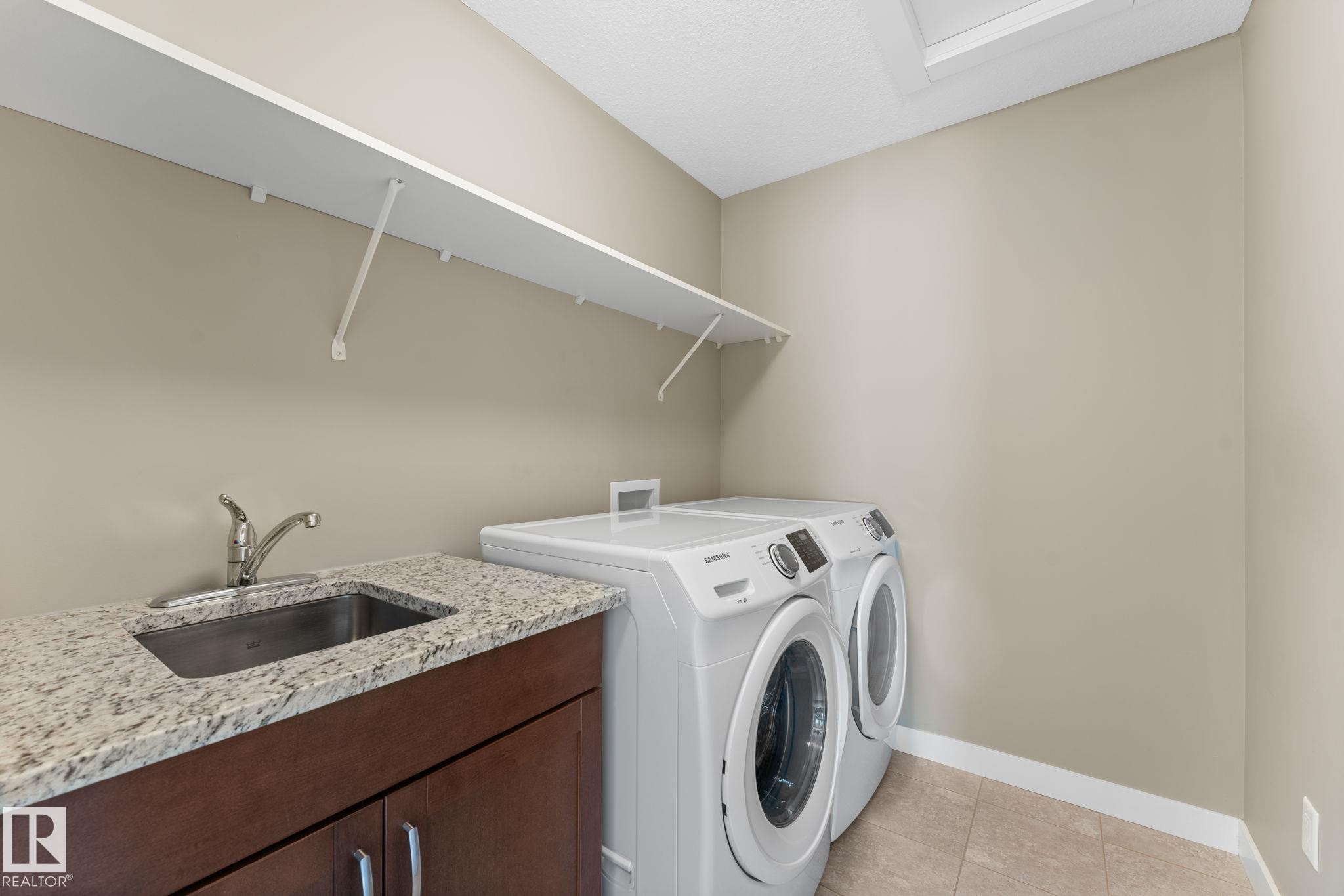 Laundry area featuring a utility sink with a stainless steel faucet, a granite-finish countertop, and dark wood-finish cabinetry - 3413 Cameron Heights Cove Nw, Edmonton, AB - Indoor Photo Showing Laundry Room
