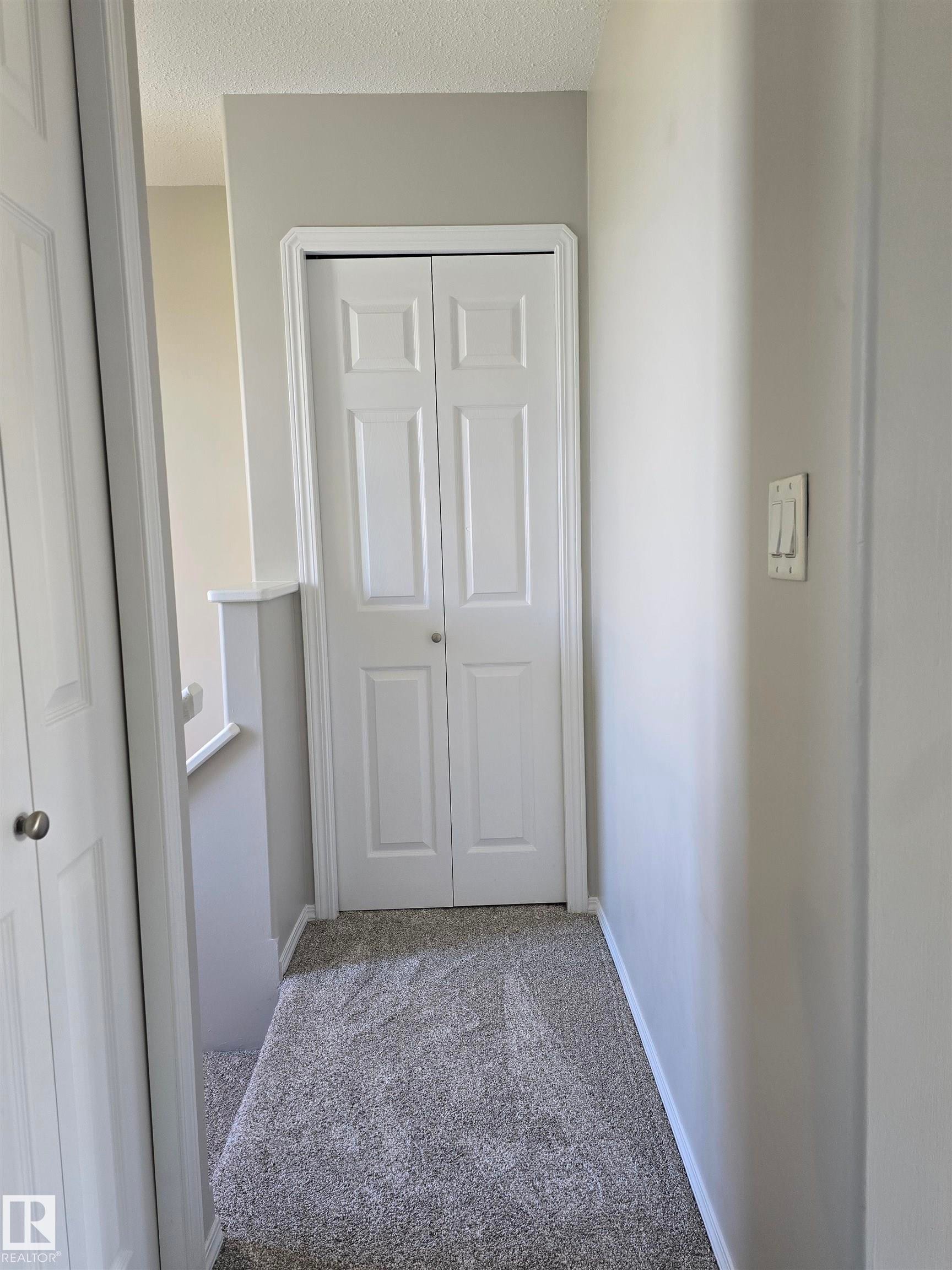 Hallway featuring light gray walls, textured carpet flooring, and white bi-fold doors - 4120 47 Street, Drayton Valley, AB - Indoor Photo Showing Other Room