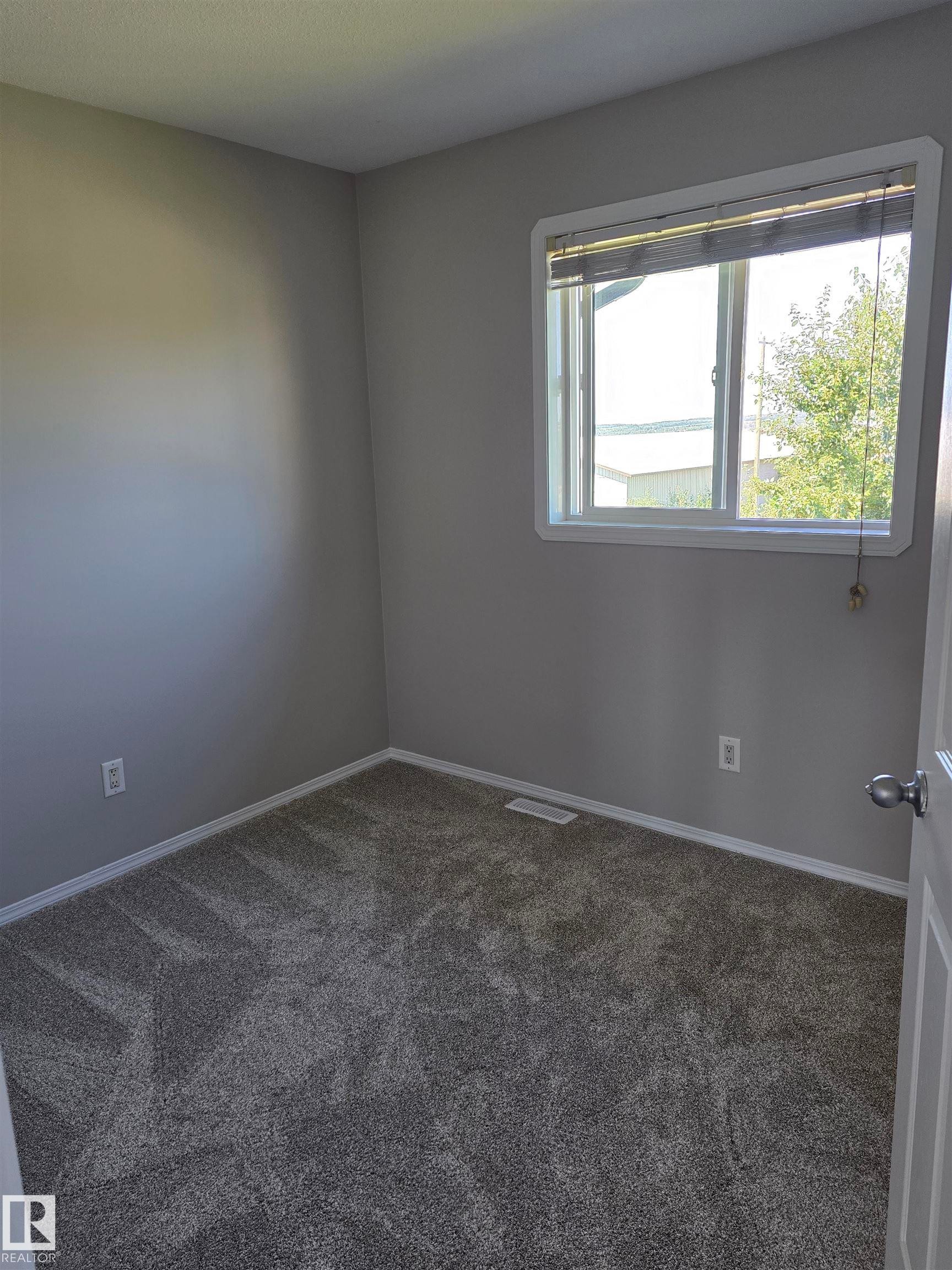 Interior room featuring neutral gray walls, a white-framed window with blinds, and dark gray patterned carpeting - 4120 47 Street, Drayton Valley, AB - Indoor Photo Showing Other Room