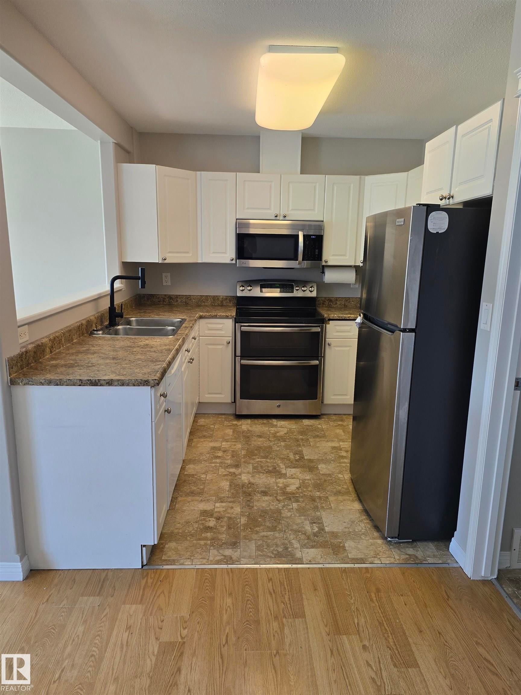 U-shaped kitchen featuring white cabinetry, stone-finish countertops, stainless steel appliances, and tile-look flooring - 4120 47 Street, Drayton Valley, AB - Indoor Photo Showing Kitchen With Double Sink