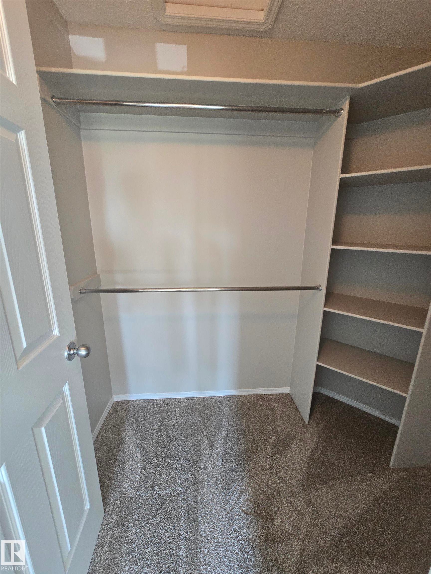 Walk-in closet featuring built-in shelving, two clothing rods, and carpeting - 4120 47 Street, Drayton Valley, AB - Indoor With Storage