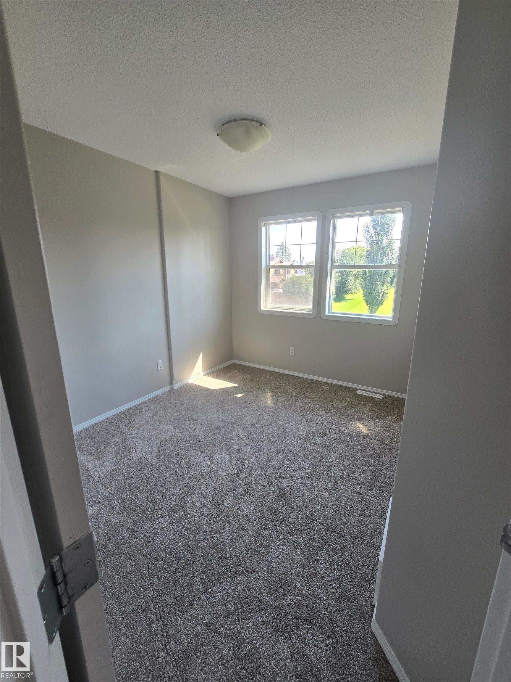 Spacious room featuring neutral carpeting, light gray walls, a flush-mount ceiling light, and two large windows - 4120 47 Street, Drayton Valley, AB - Indoor Photo Showing Other Room