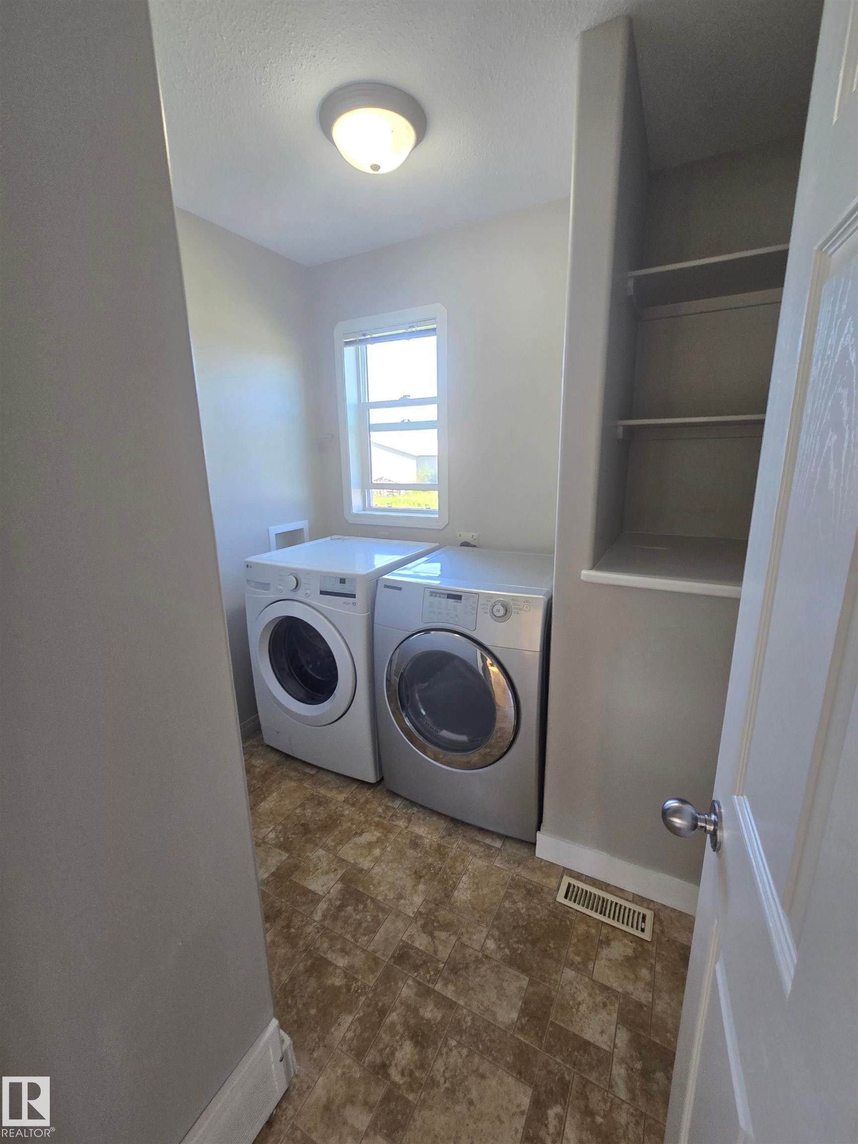 Dedicated laundry space featuring a window, built-in shelving, and patterned vinyl flooring - 4120 47 Street, Drayton Valley, AB - Indoor Photo Showing Laundry Room